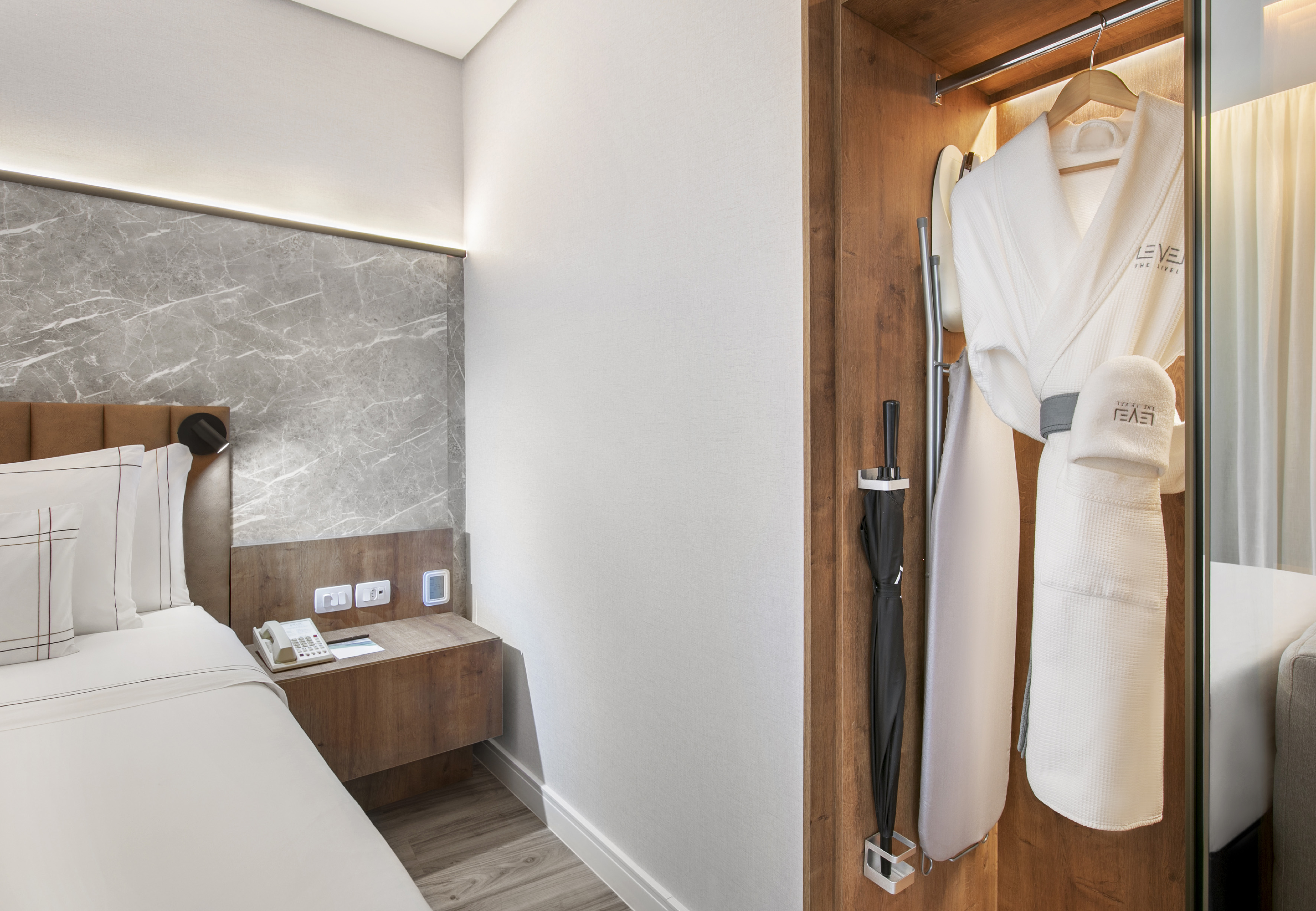 Modern hotel bedroom with nightstand, wardrobe, bathrobe, and umbrella.