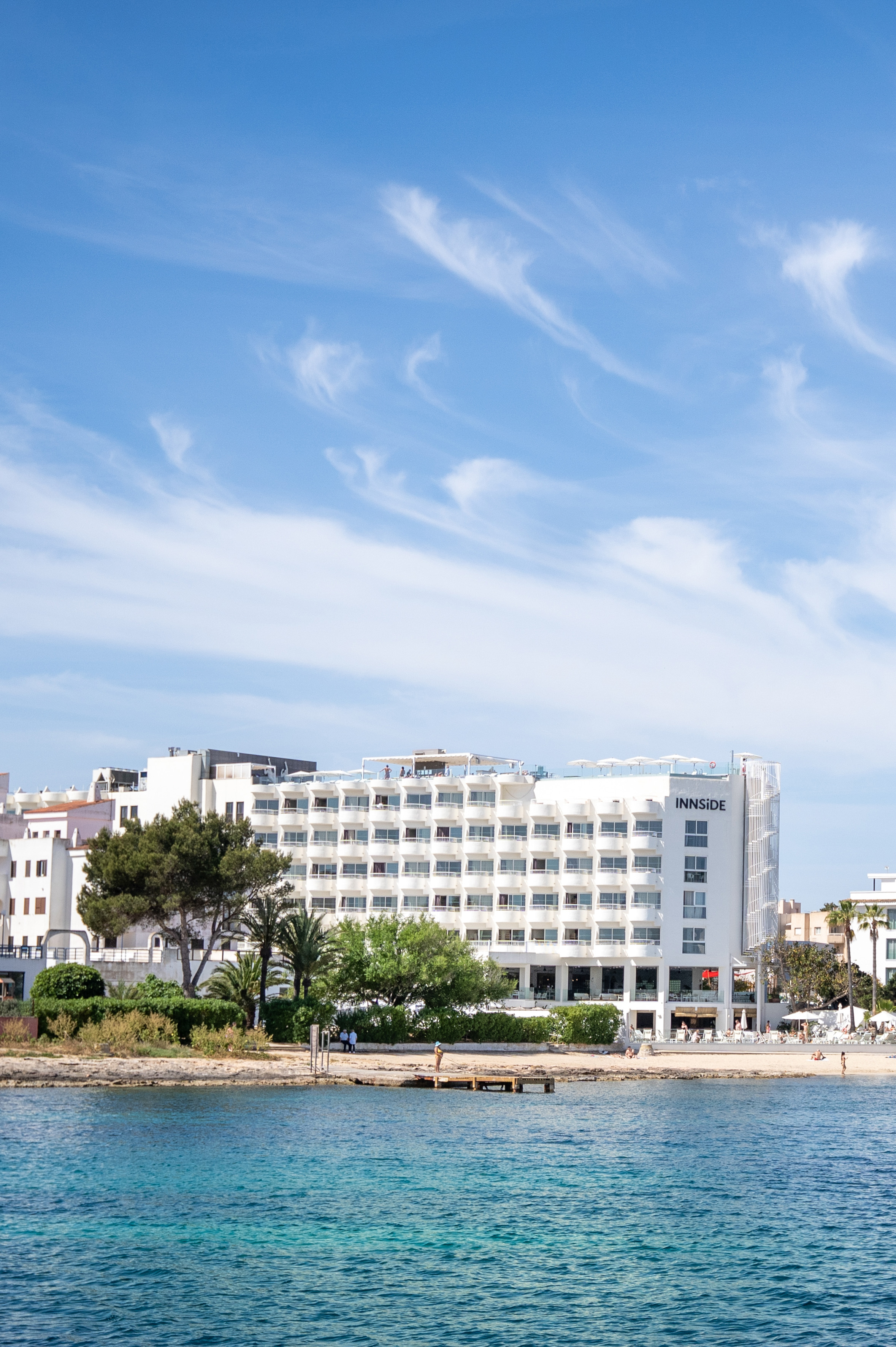 Waterfront INNSIDE resort with white facade, clear blue sea, and beach.