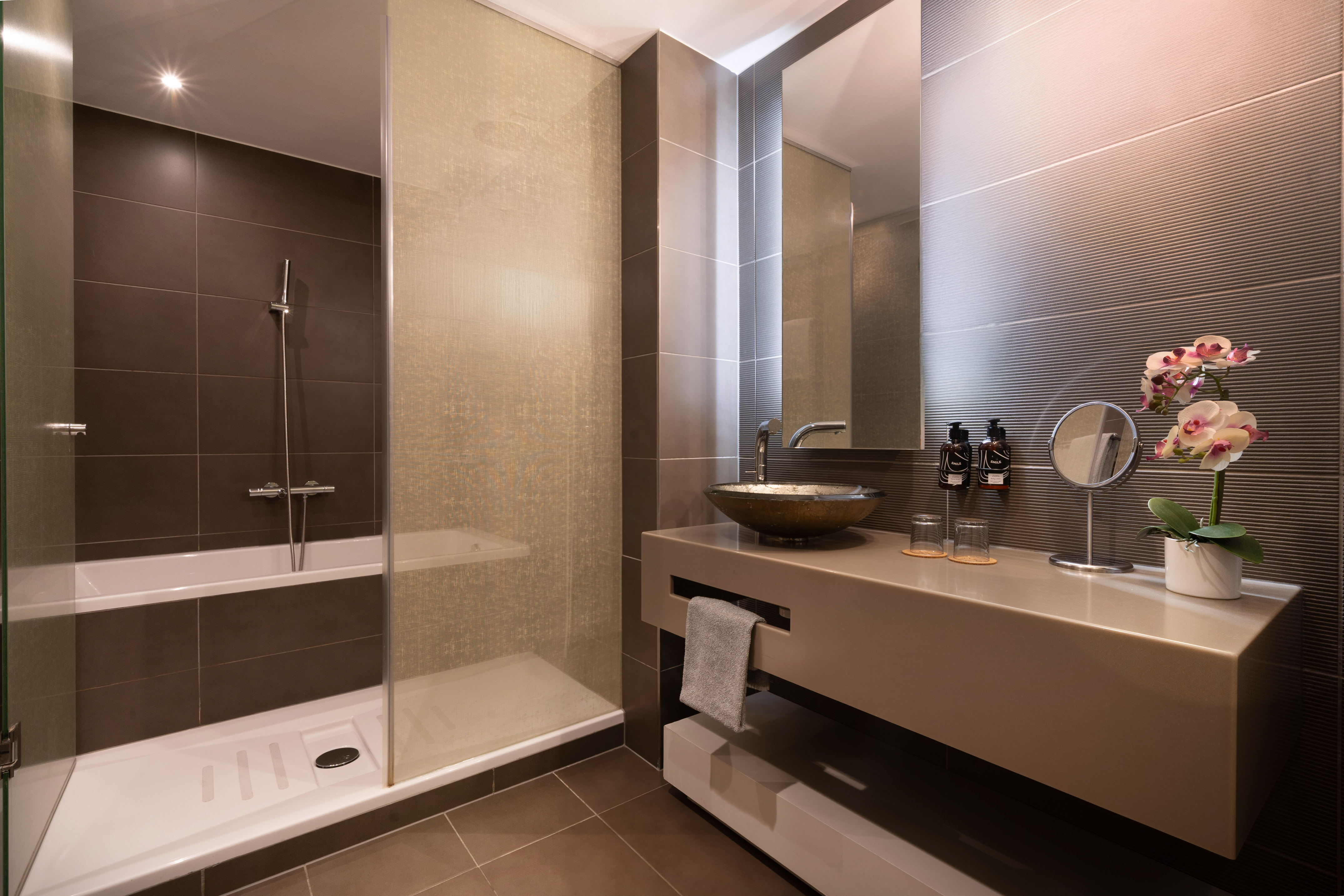 Modern bathroom with walk-in shower, bathtub, vessel sink, and orchid.