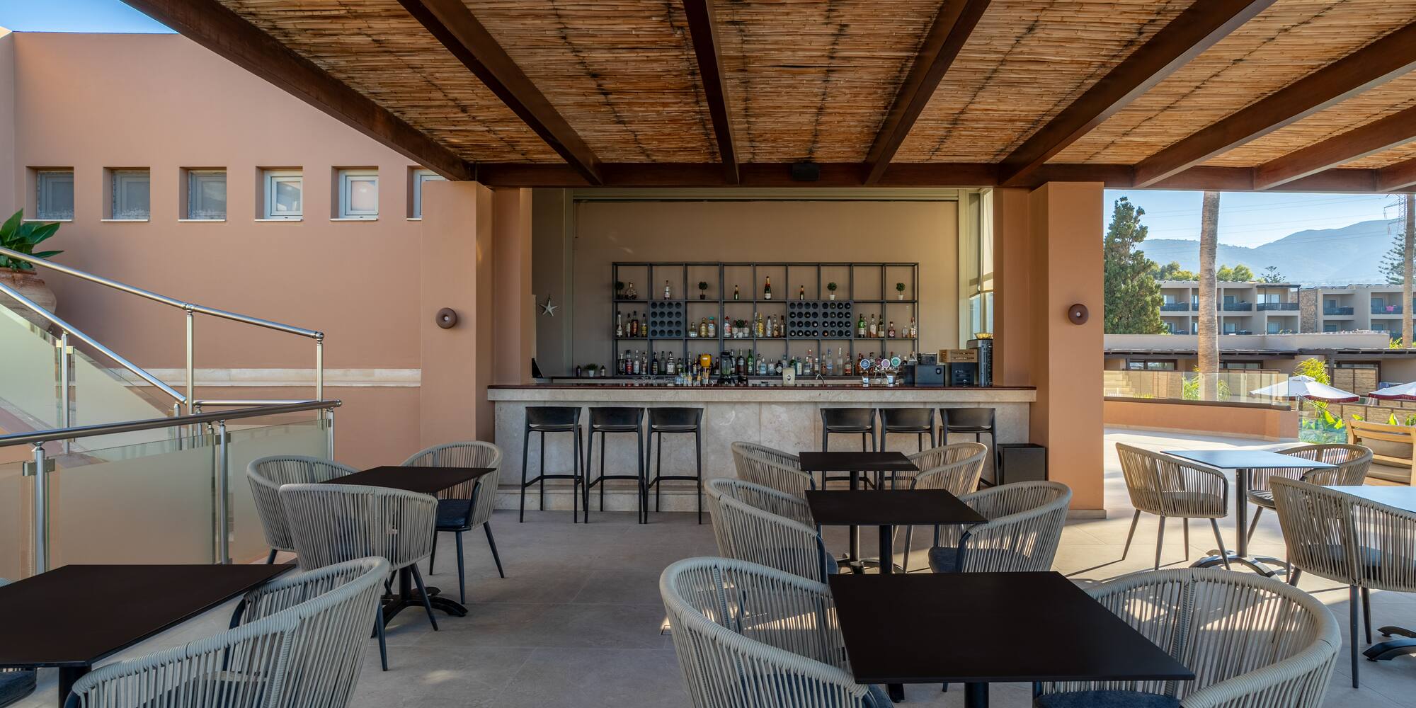 Outdoor resort bar with bamboo ceiling, modern seating, and distant mountain views.