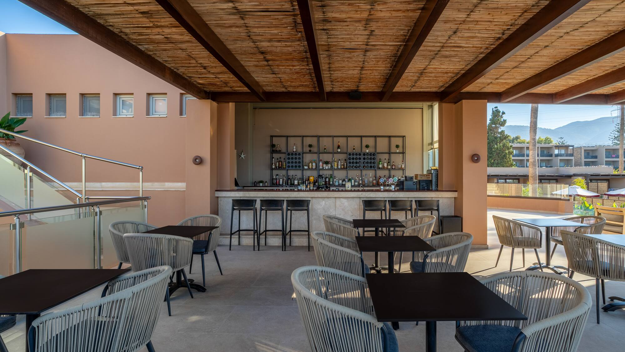 Outdoor resort bar with bamboo ceiling, modern seating, and distant mountain views.
