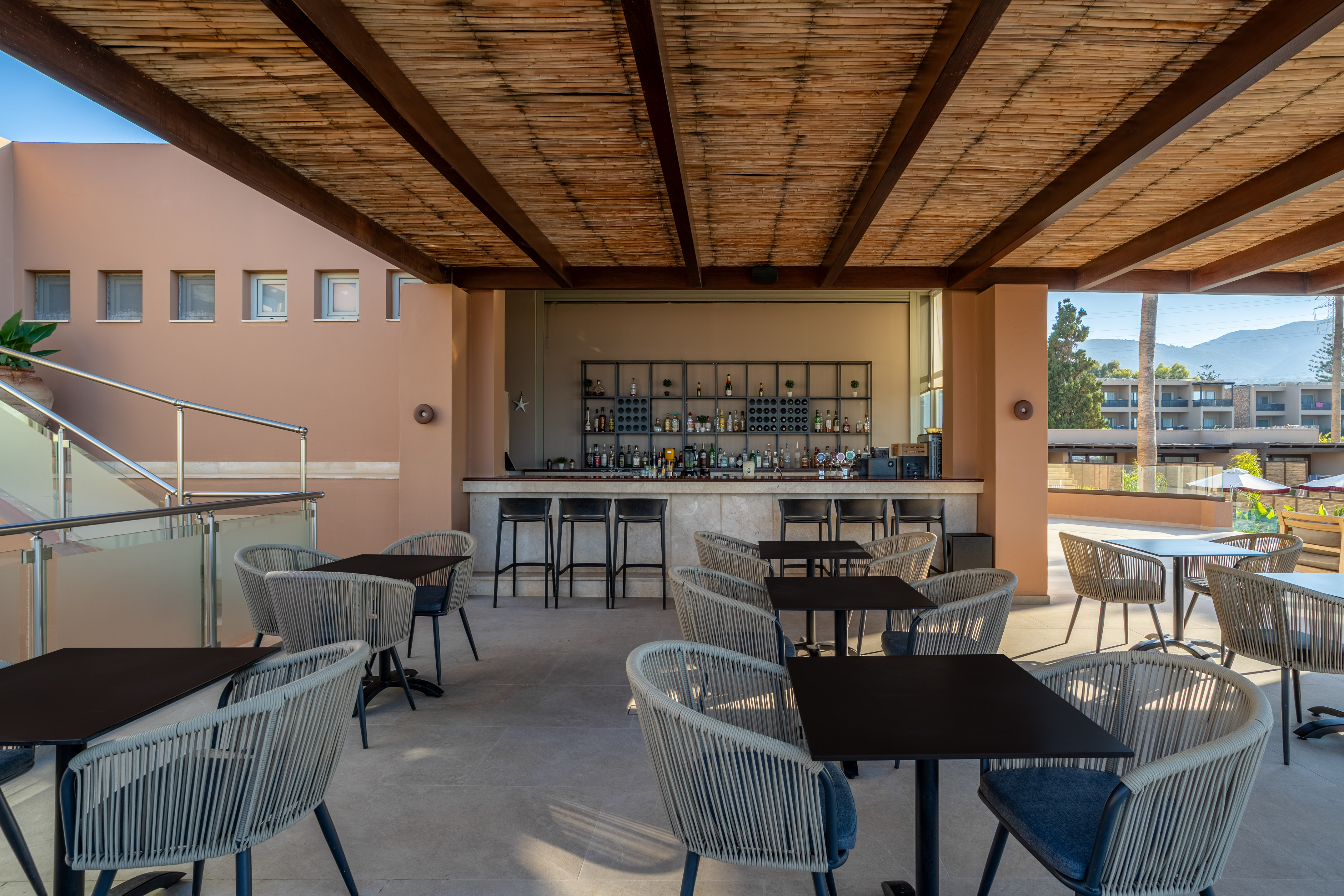Outdoor resort bar with bamboo ceiling, modern seating, and distant mountain views.