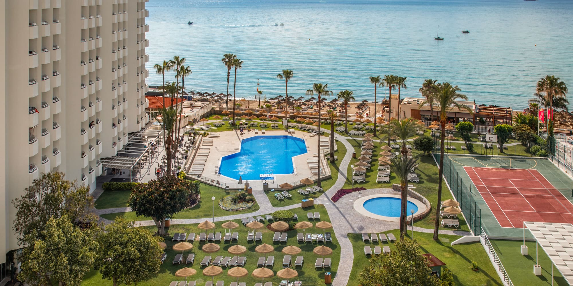 Oceanfront resort with hotel, pools, sunny beach, palm trees, and tennis court.