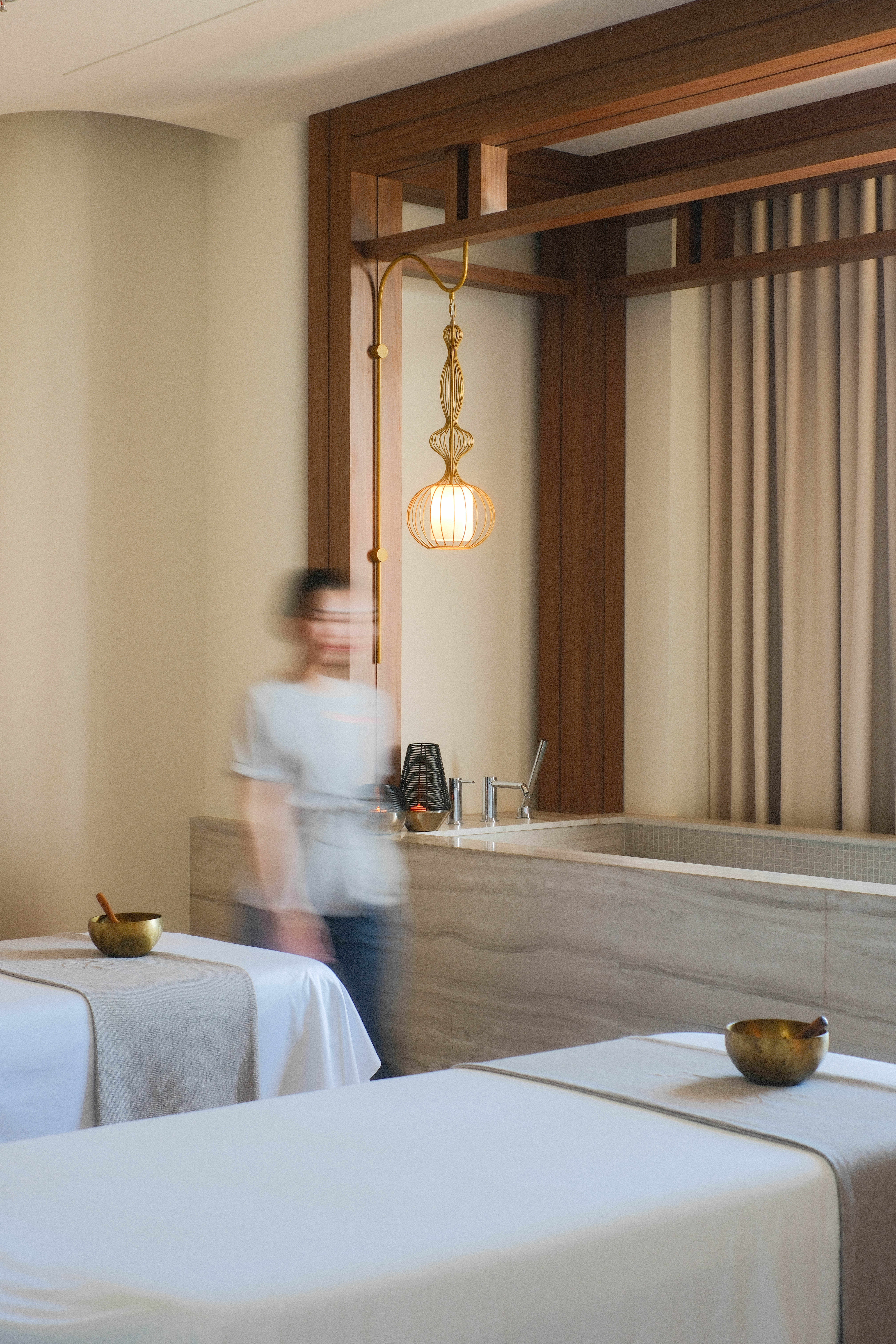 Serene spa with two massage beds, singing bowls, modern bath, and blurred staff.