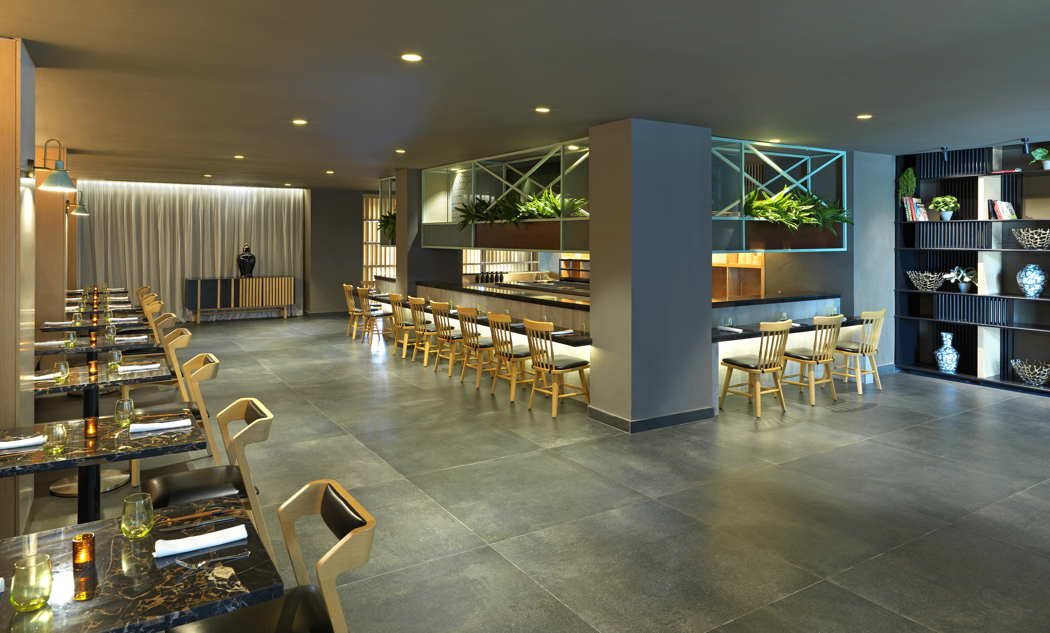 Modern restaurant with stylish dining tables, bar area, and decorative shelving.