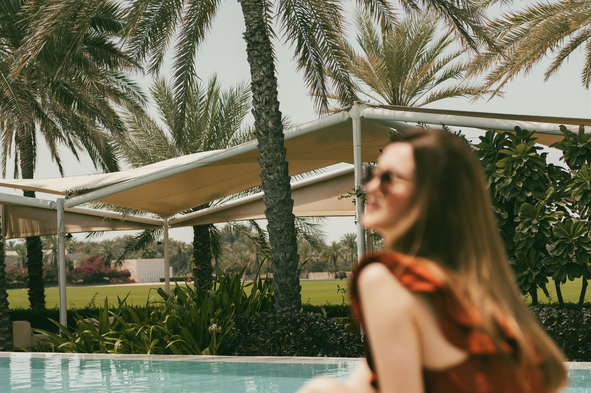 Woman at luxury resort pool, relaxing among tall palm trees.