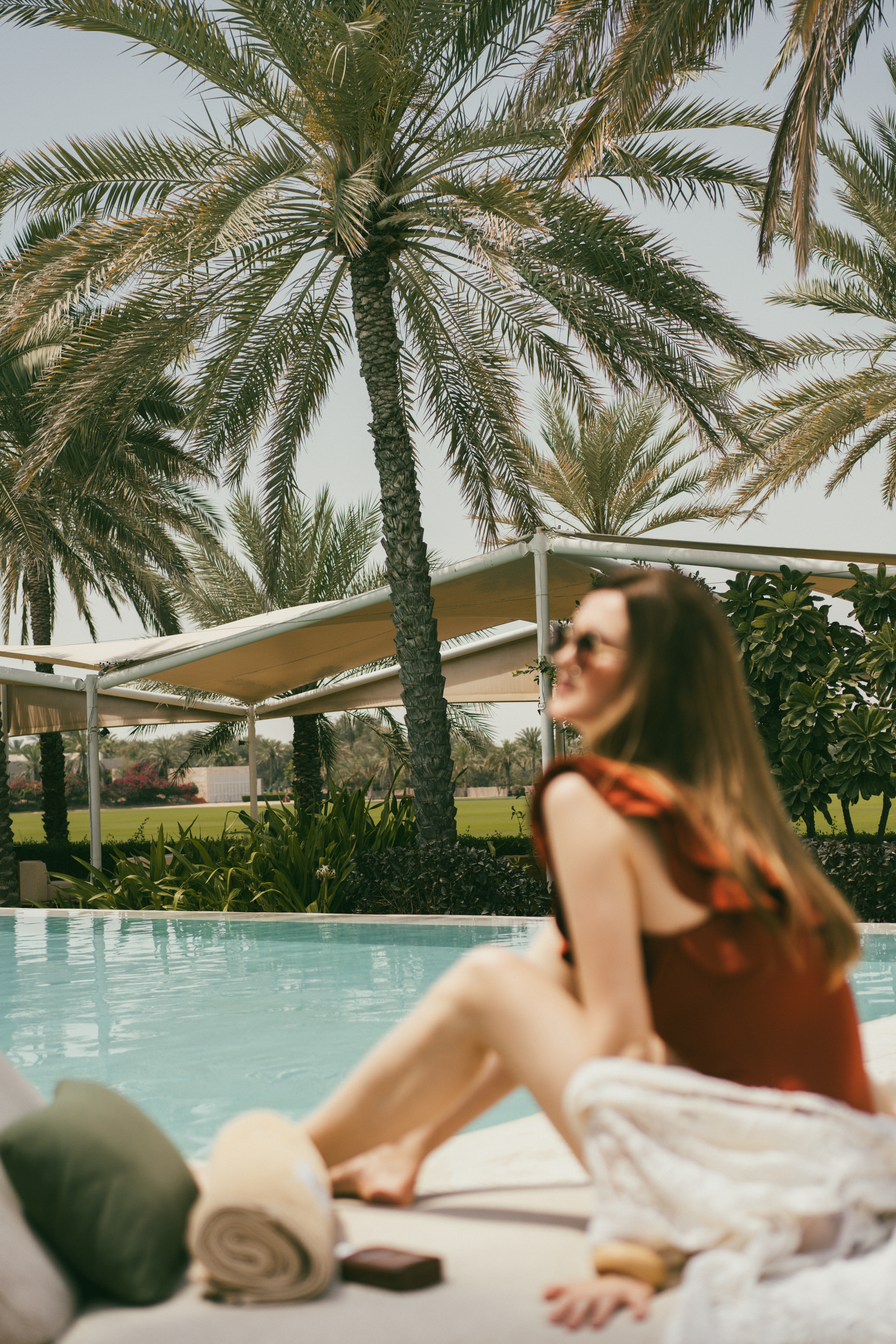 Woman at luxury resort pool, relaxing among tall palm trees.
