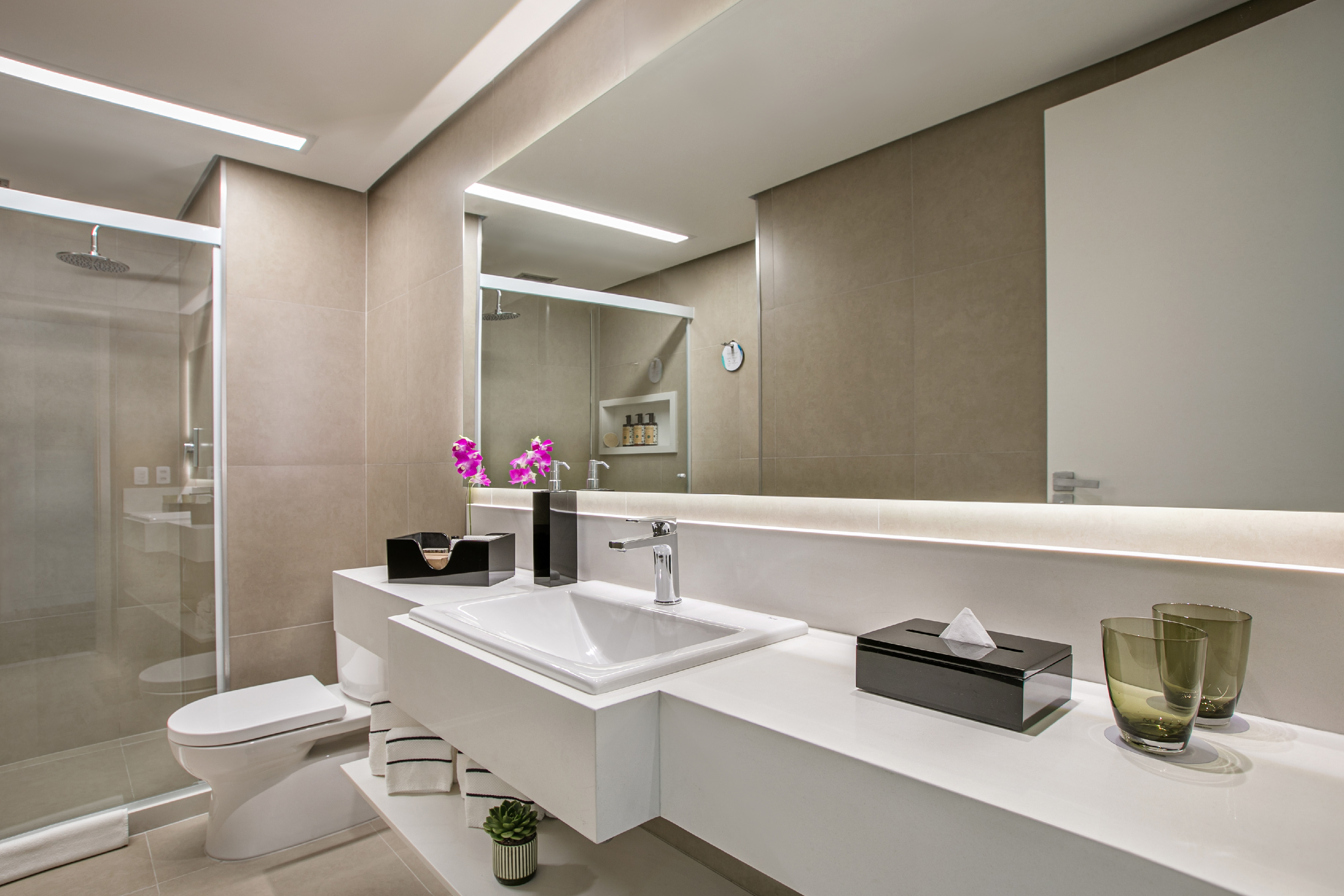 Modern hotel bathroom with floating vanity, backlit mirror, and glass shower.