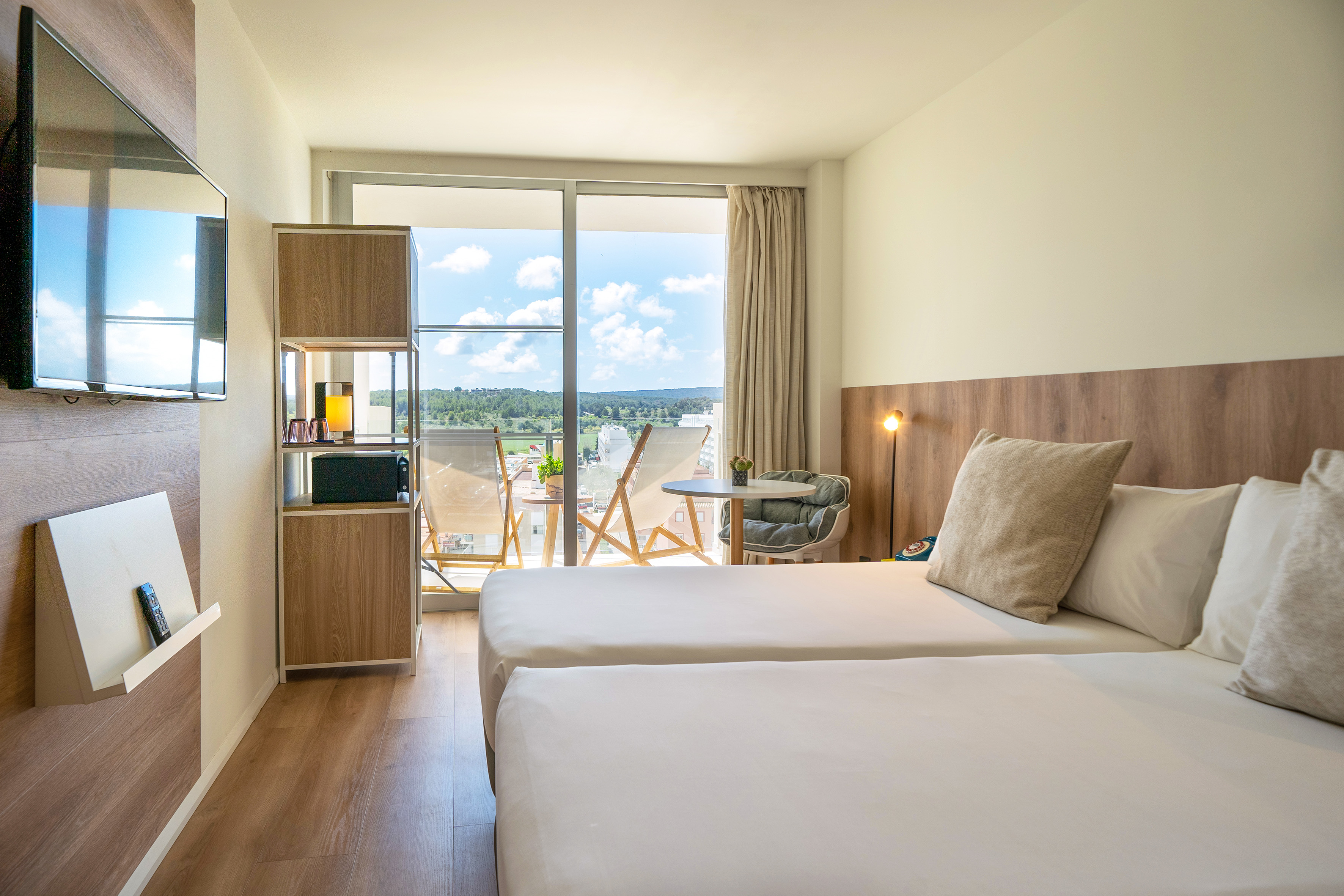 Modern hotel room with twin beds, balcony, and scenic landscape view.