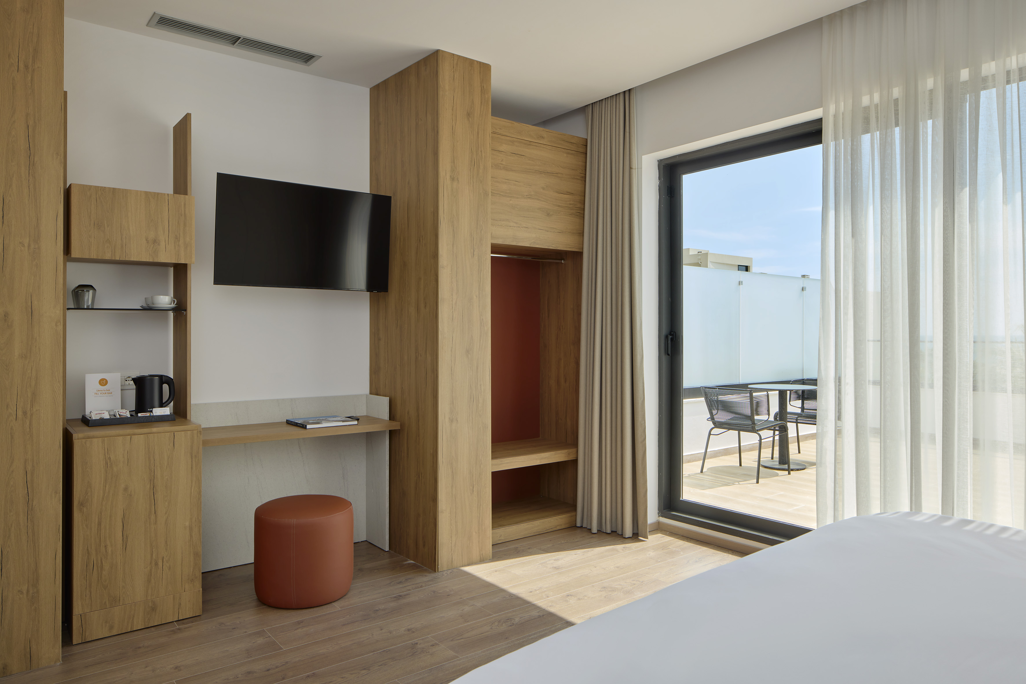Modern hotel room with private balcony, wooden desk, TV, and contemporary decor.
