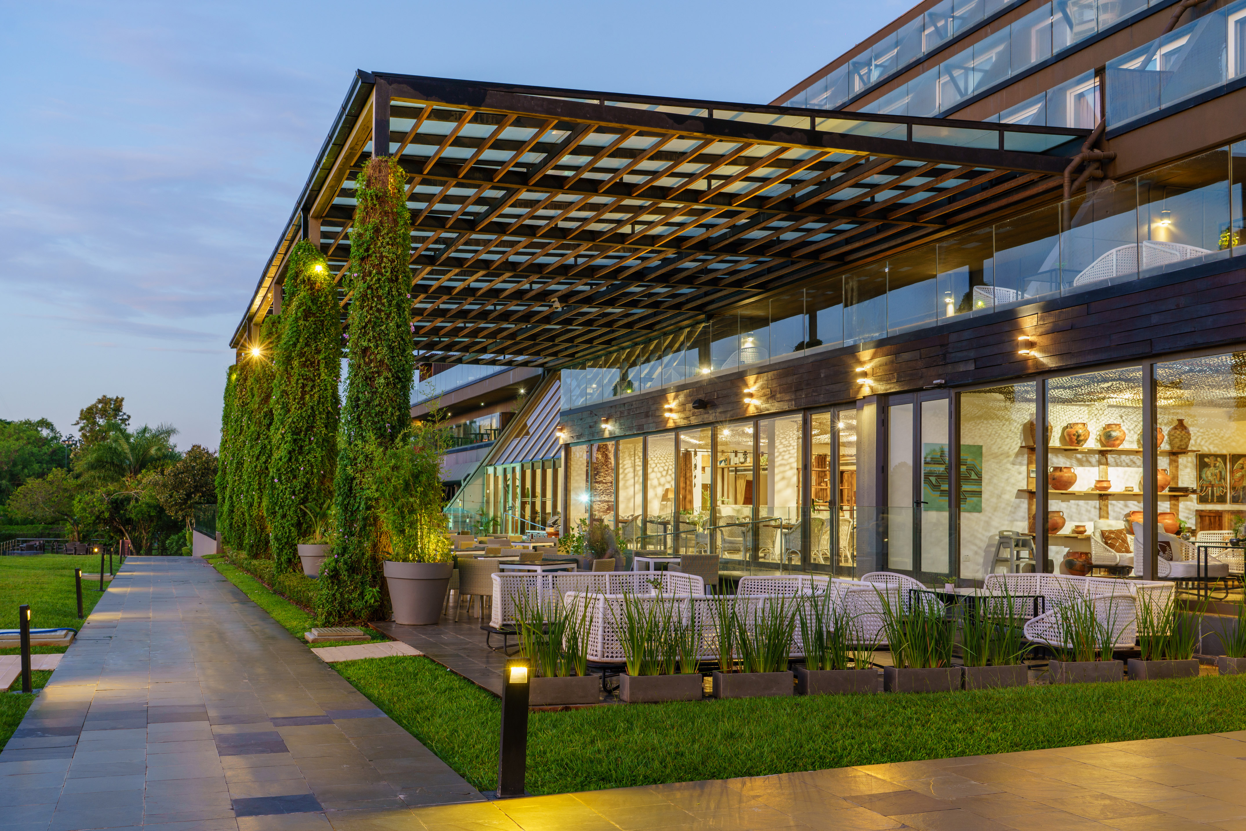Modern hotel outdoor dining patio with white furniture, pergola, and lush plants.