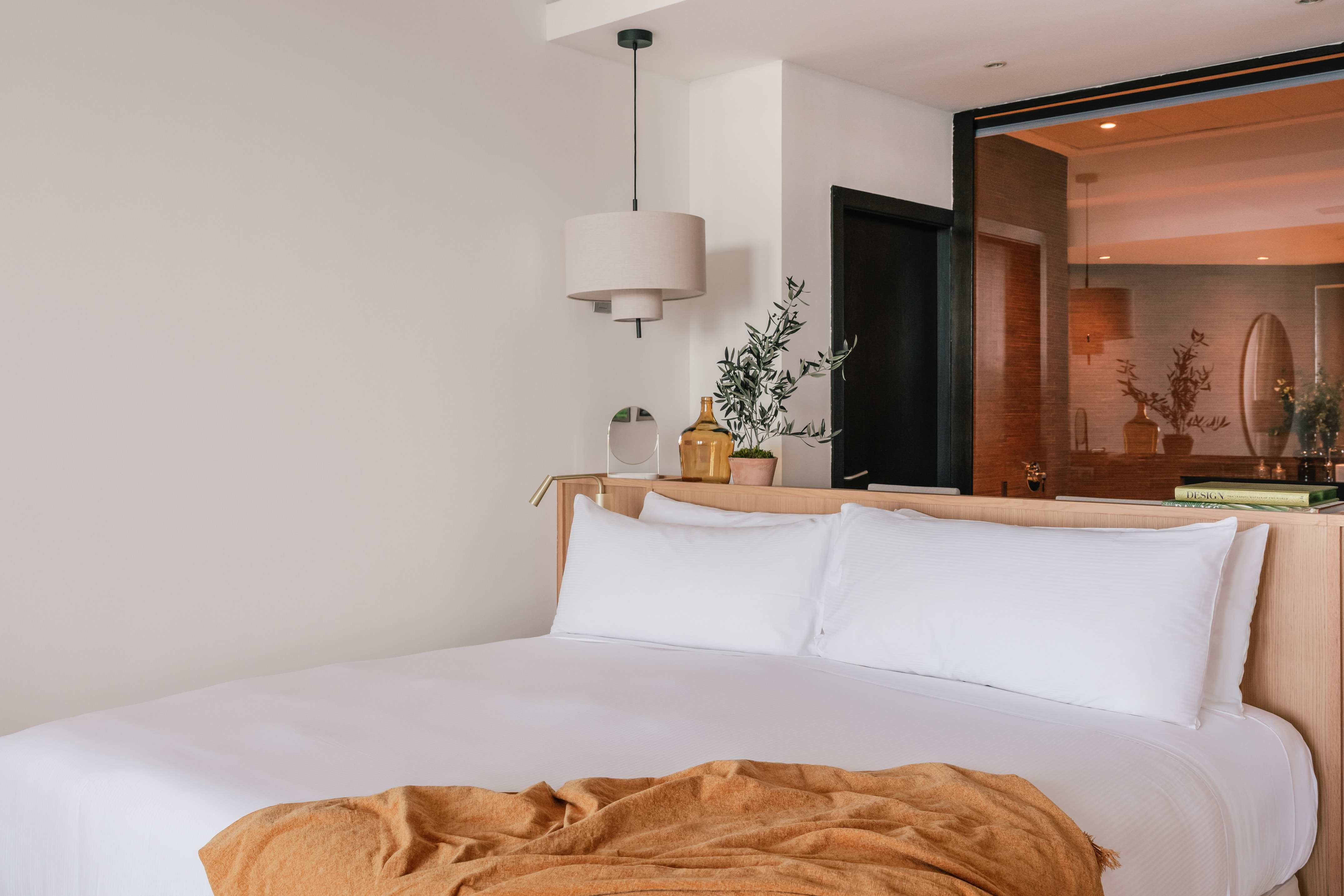 Modern bedroom with white bed, amber throw, wood headboard, and pendant lamp.