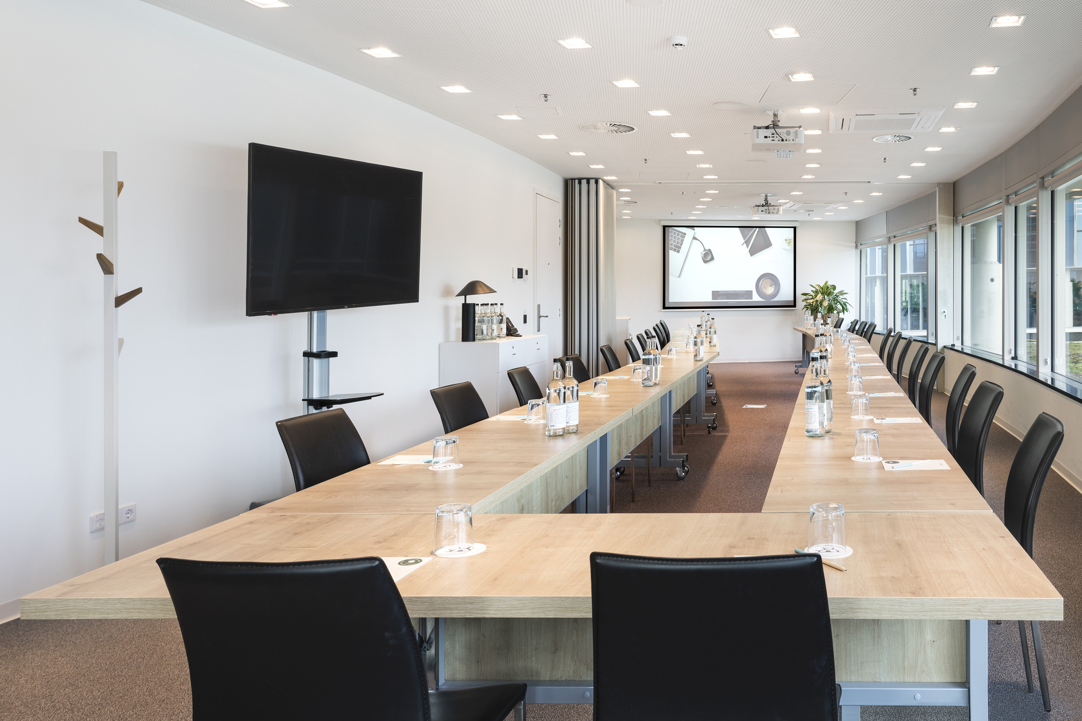 Modern U-shaped meeting room with TV and projector screen.