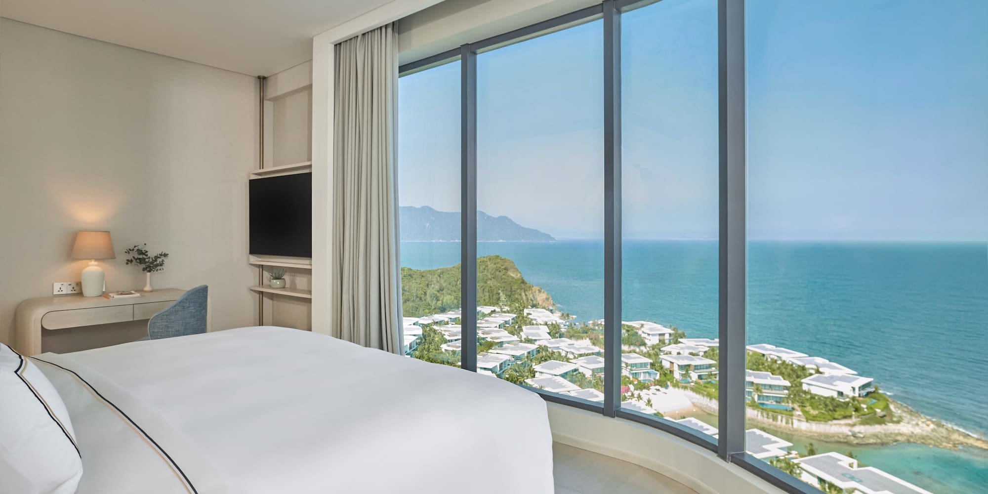 Modern hotel bedroom with curved panoramic ocean view, coastal resort.