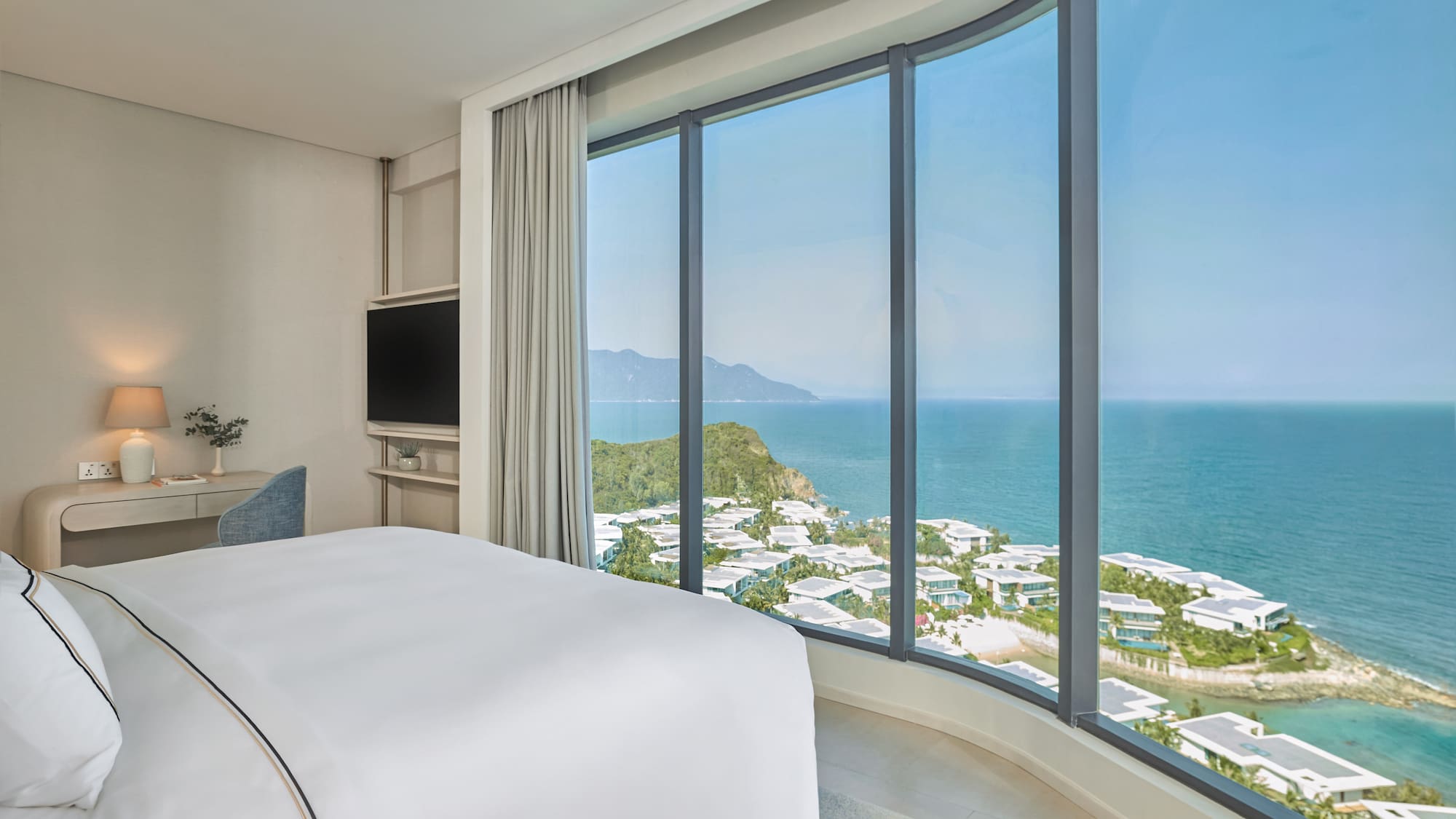 Modern hotel bedroom with curved panoramic ocean view, coastal resort.