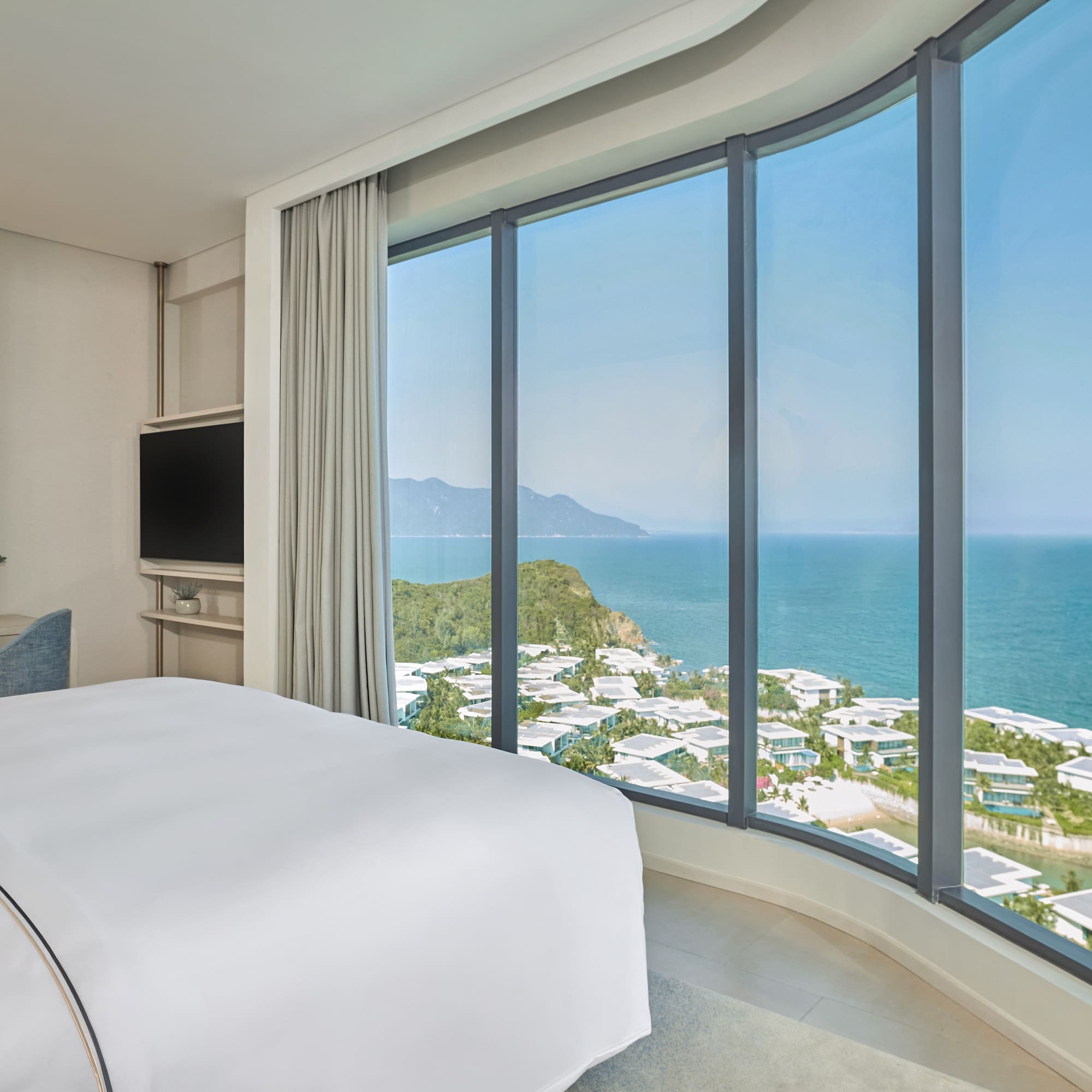 Modern hotel bedroom with curved panoramic ocean view, coastal resort.