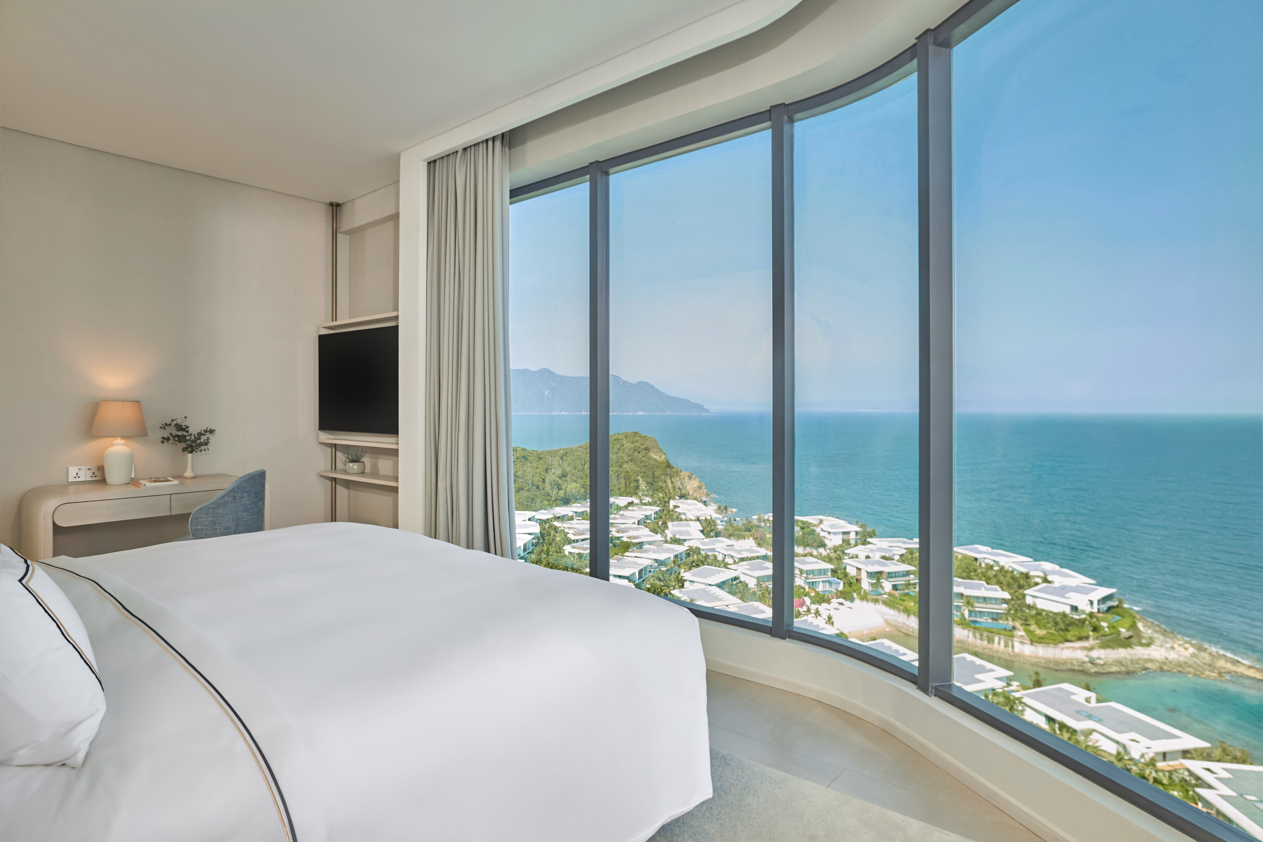 Modern hotel bedroom with curved panoramic ocean view, coastal resort.