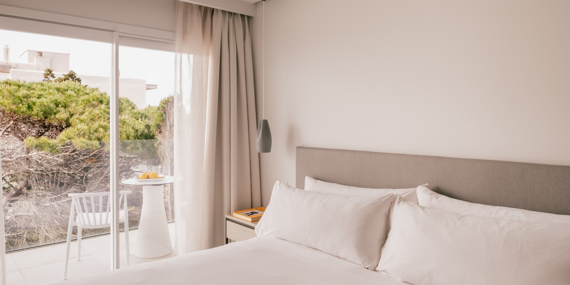 Modern bedroom with white bed, balcony, and green view.