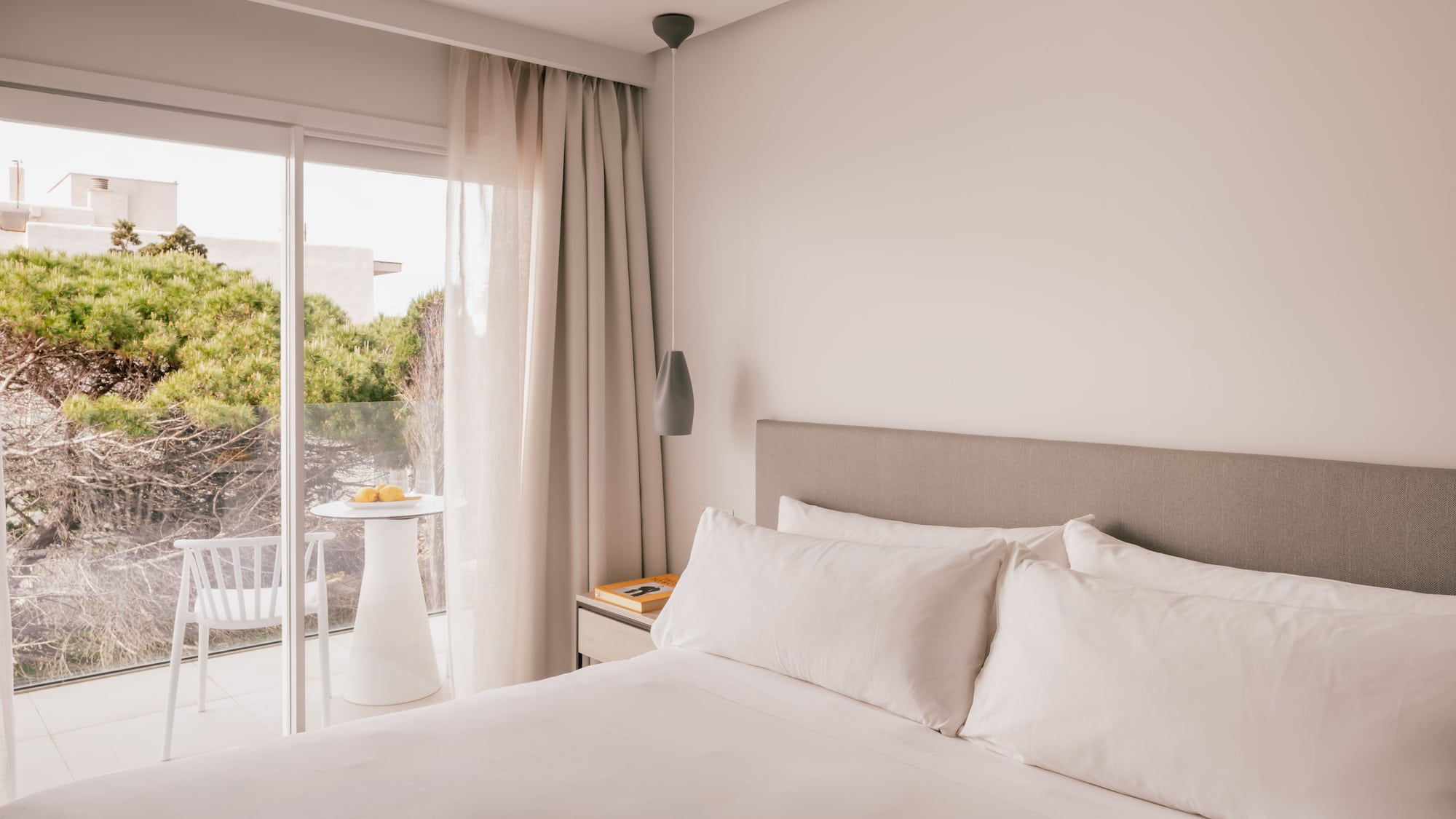 Modern bedroom with white bed, balcony, and green view.