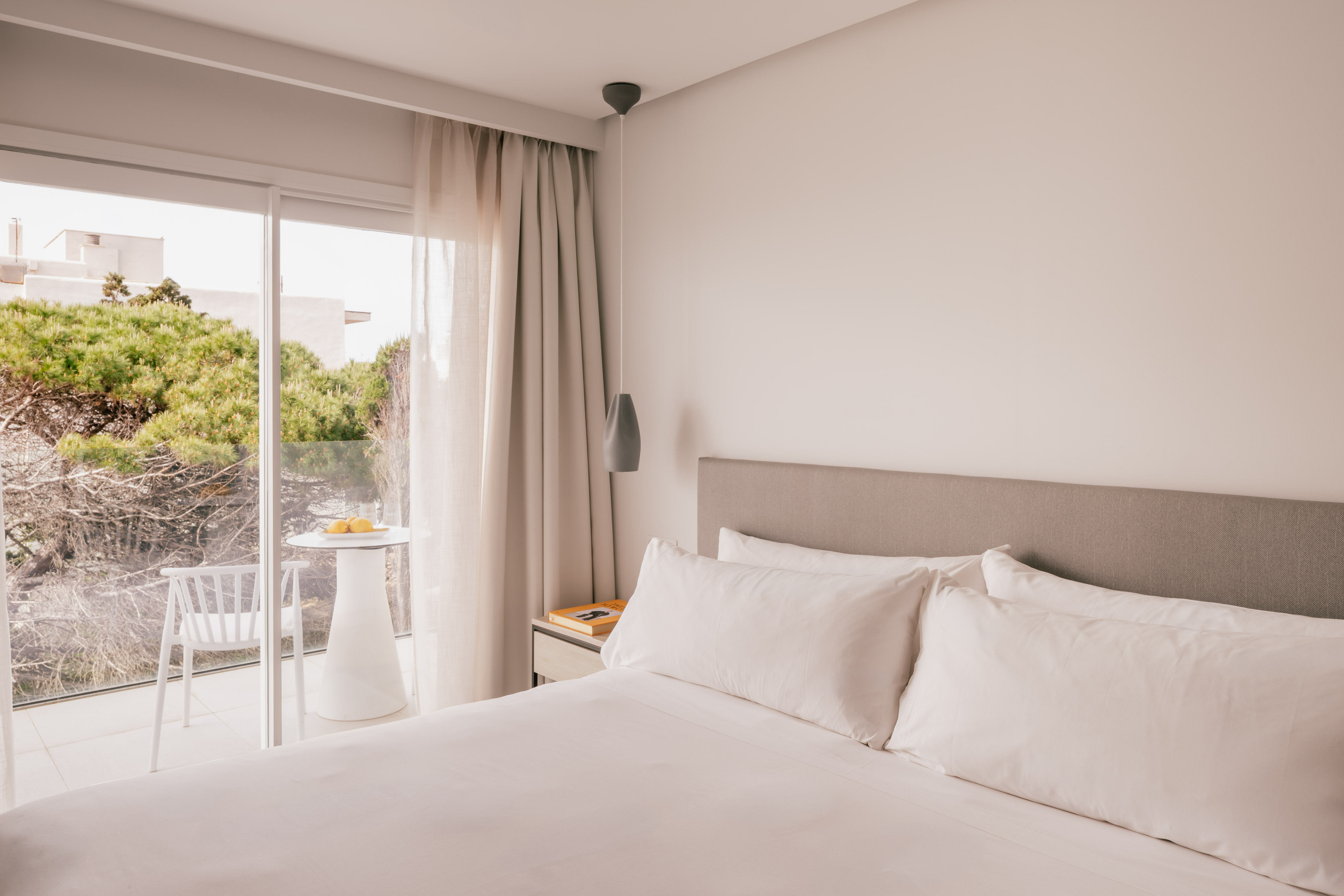 Habitación moderna de hotel con cama grande, balcón y vista a la naturaleza.