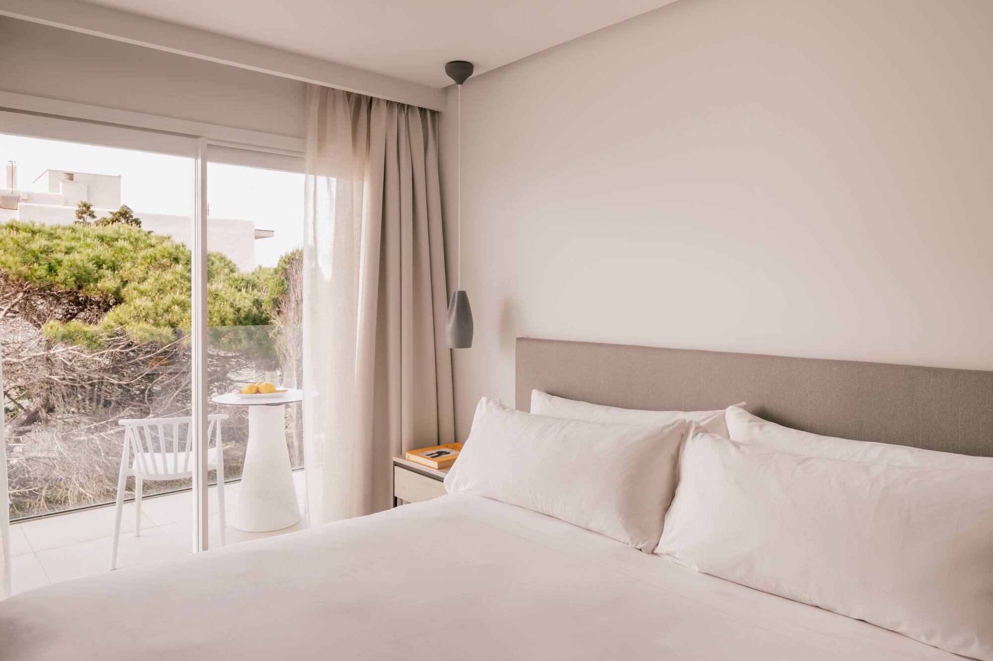 Habitación moderna de hotel con cama grande, balcón y vista a la naturaleza.