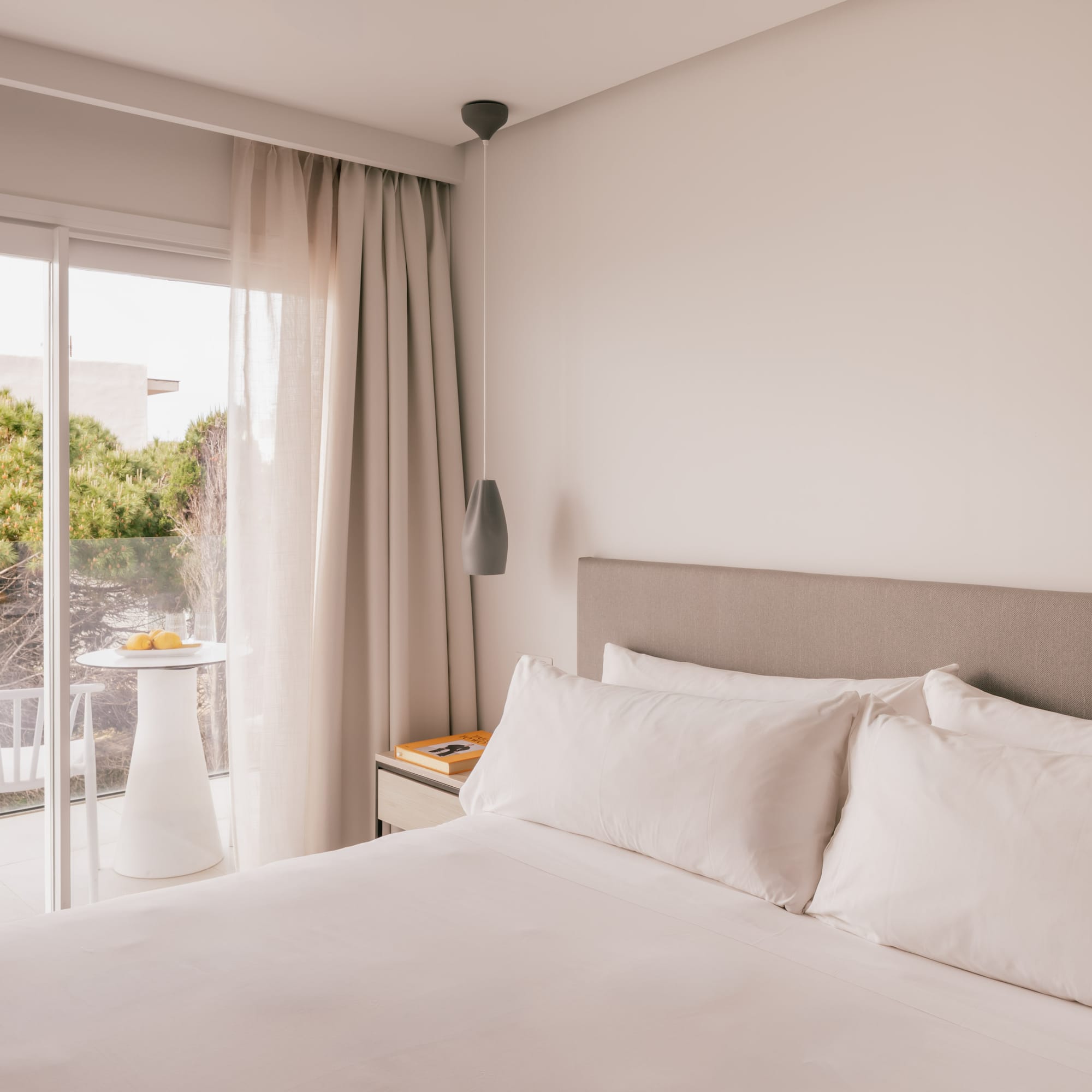 Modern bedroom with white bed, balcony, and green view.