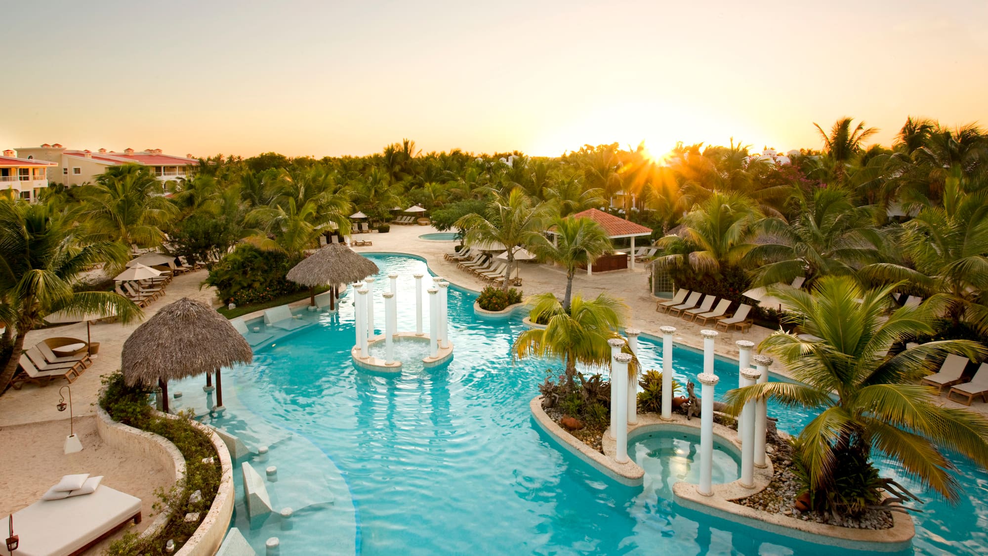 a pool with palm trees and a sun setting