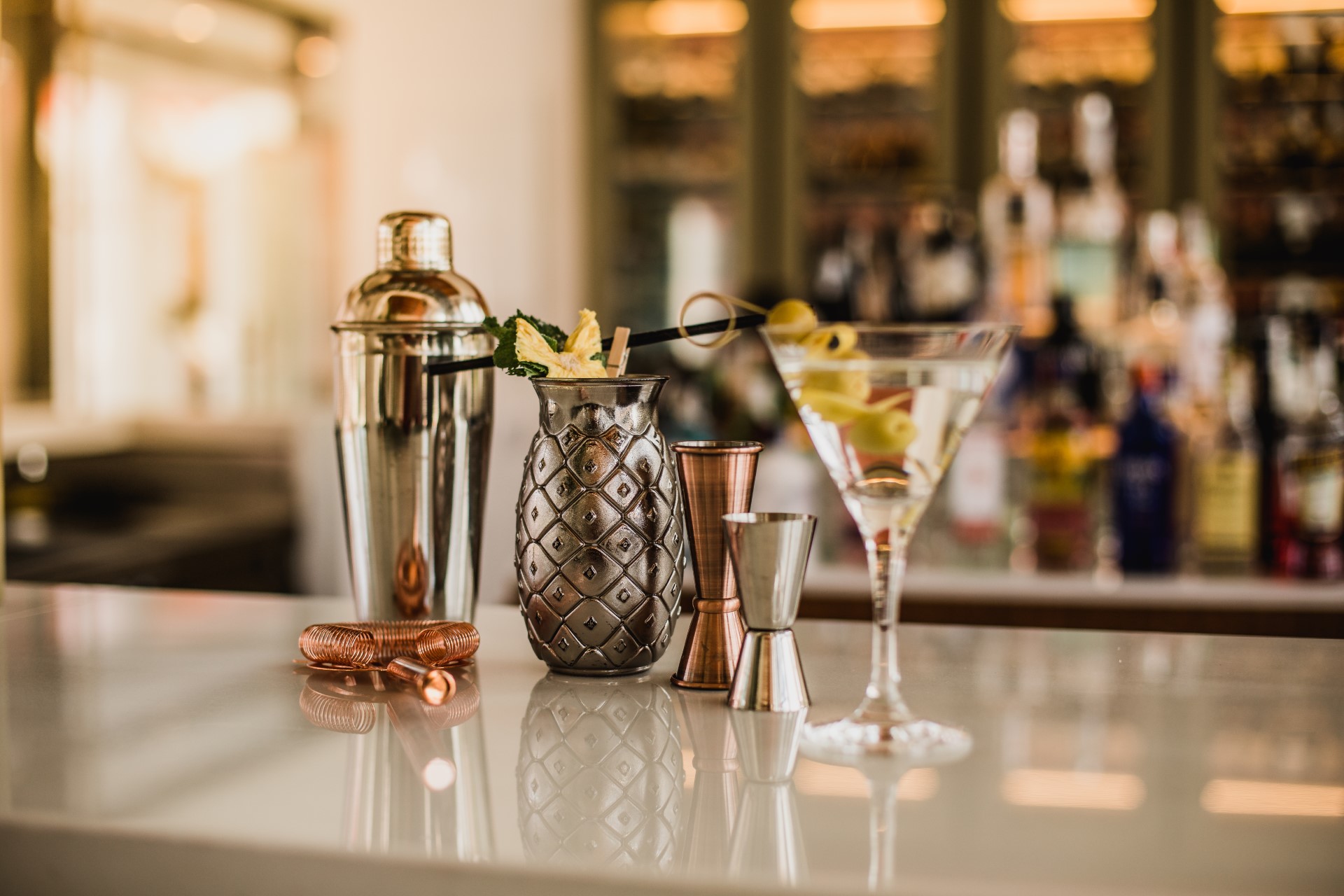 Mixology bar tools: shaker, pineapple cup, jiggers, and martini glass.