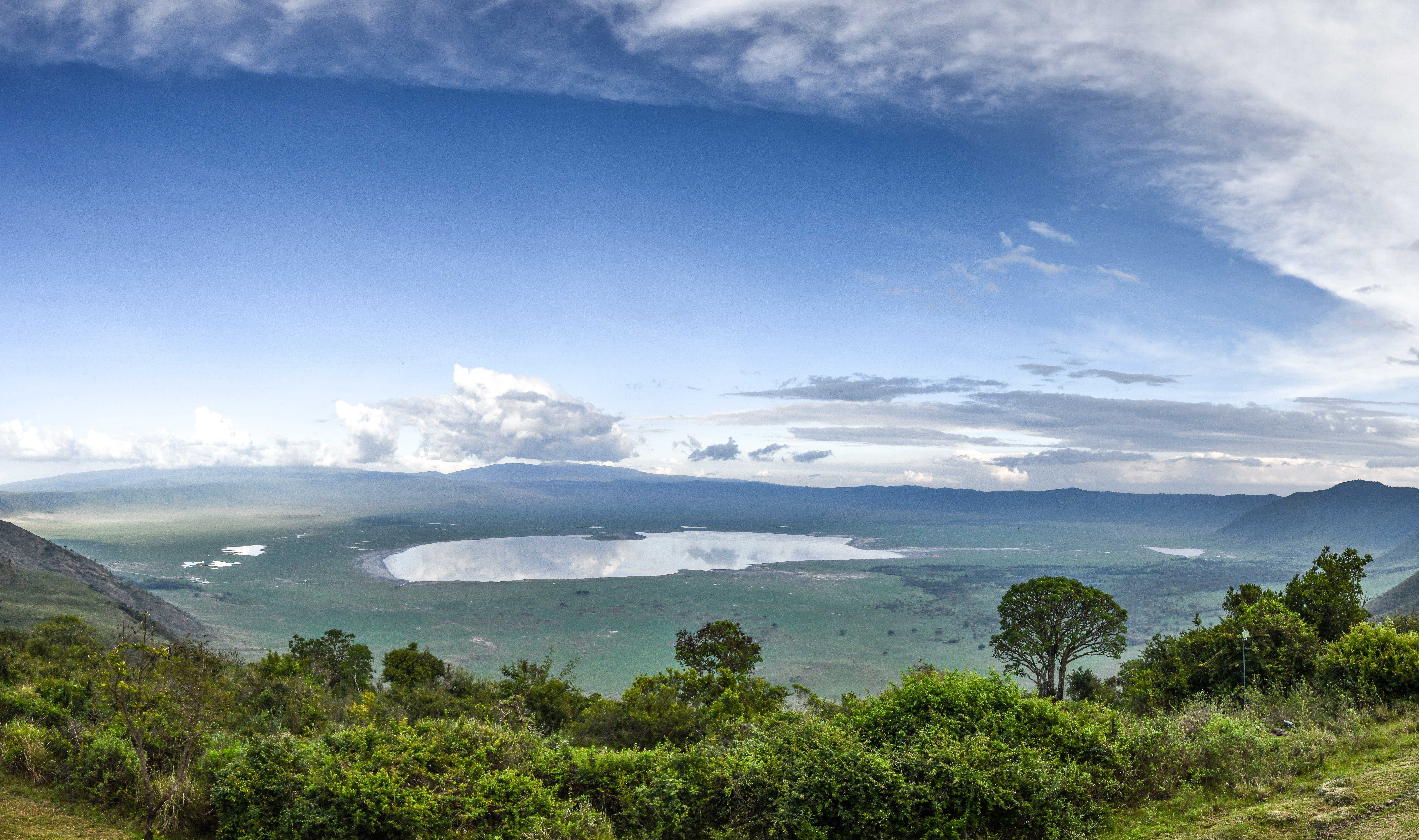 Ngorongoro Crater panoramic view with lake reflecting sky, lush green landscape.