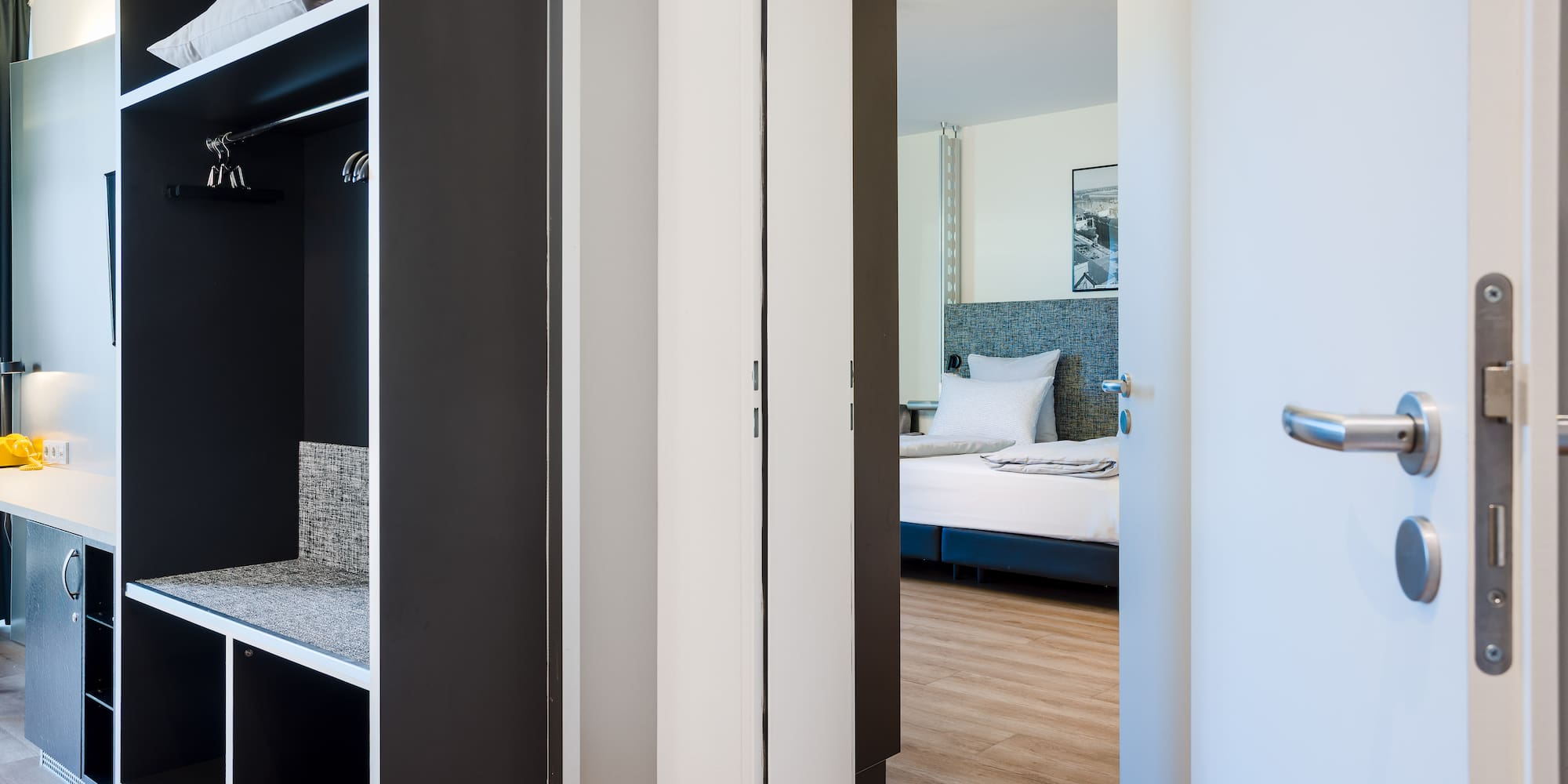 Modern hotel room entrance, open wardrobe with storage, glimpse of bedroom.