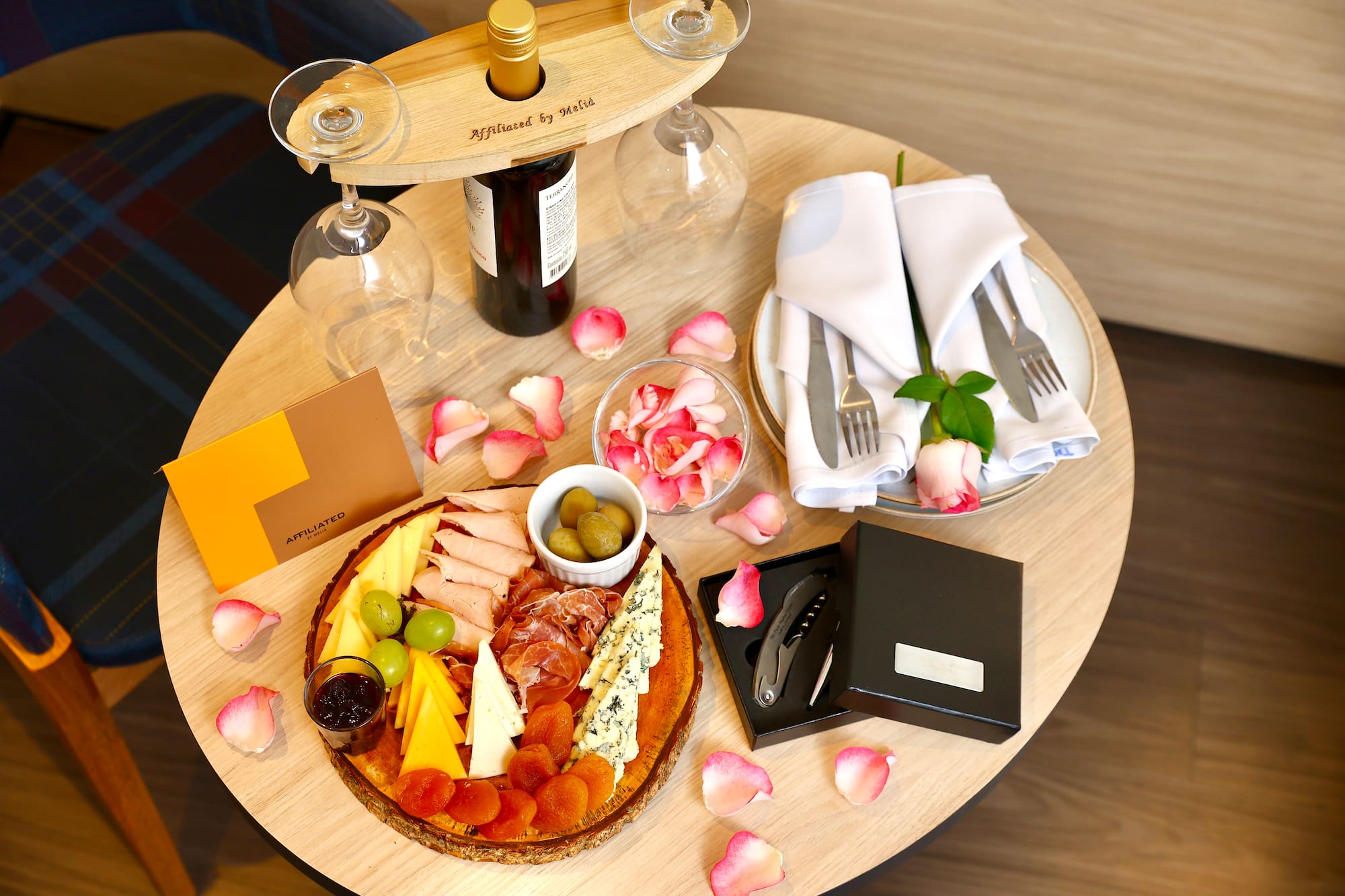 Hotel charcuterie board with wine, cheese, meats, and rose petals.