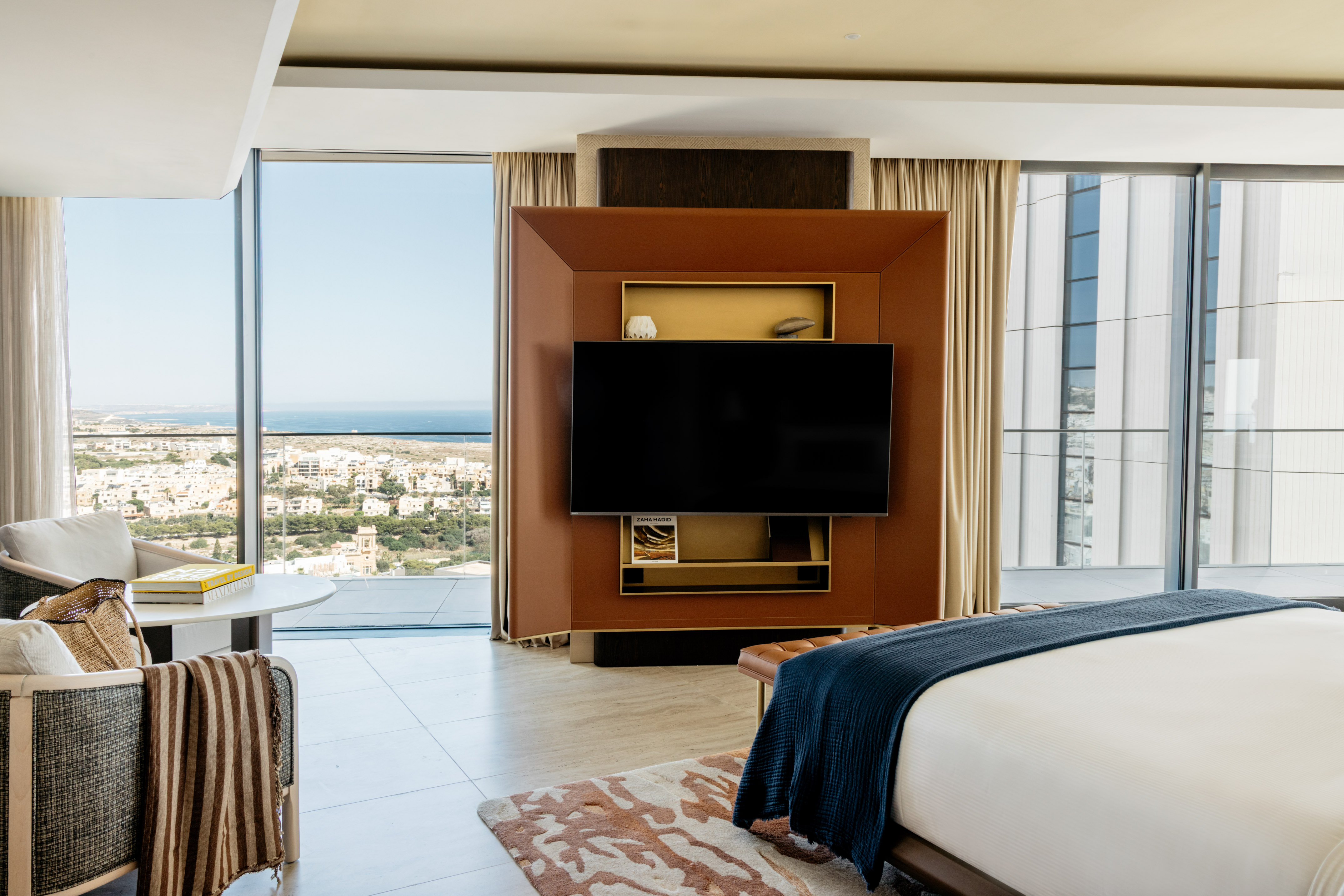 Modern luxury hotel room with ocean view, large TV, and king bed.