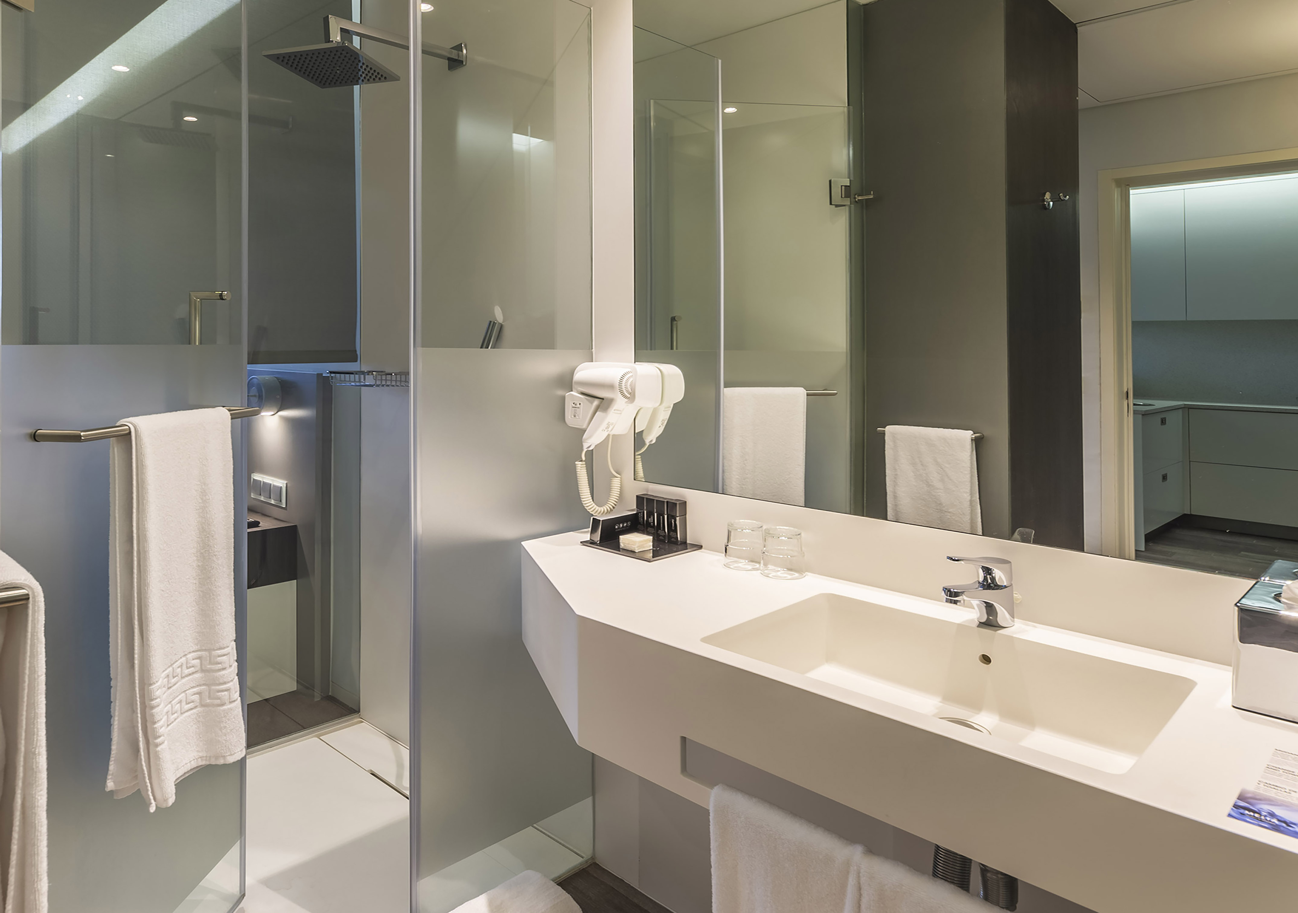 Modern hotel bathroom with glass shower, vanity sink, mirror, and hairdryer.