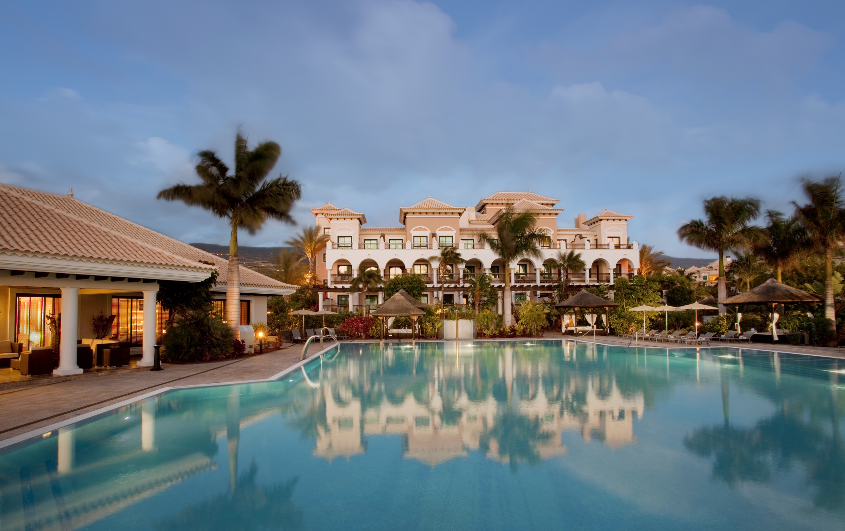 Luxury resort hotel with large swimming pool, palm trees at dusk.