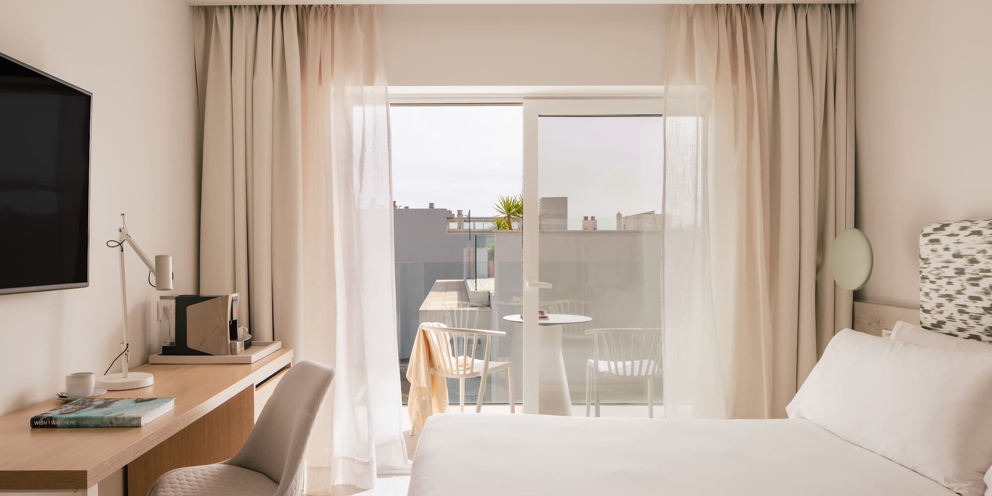 Bright, modern hotel room with bed, desk, and balcony.