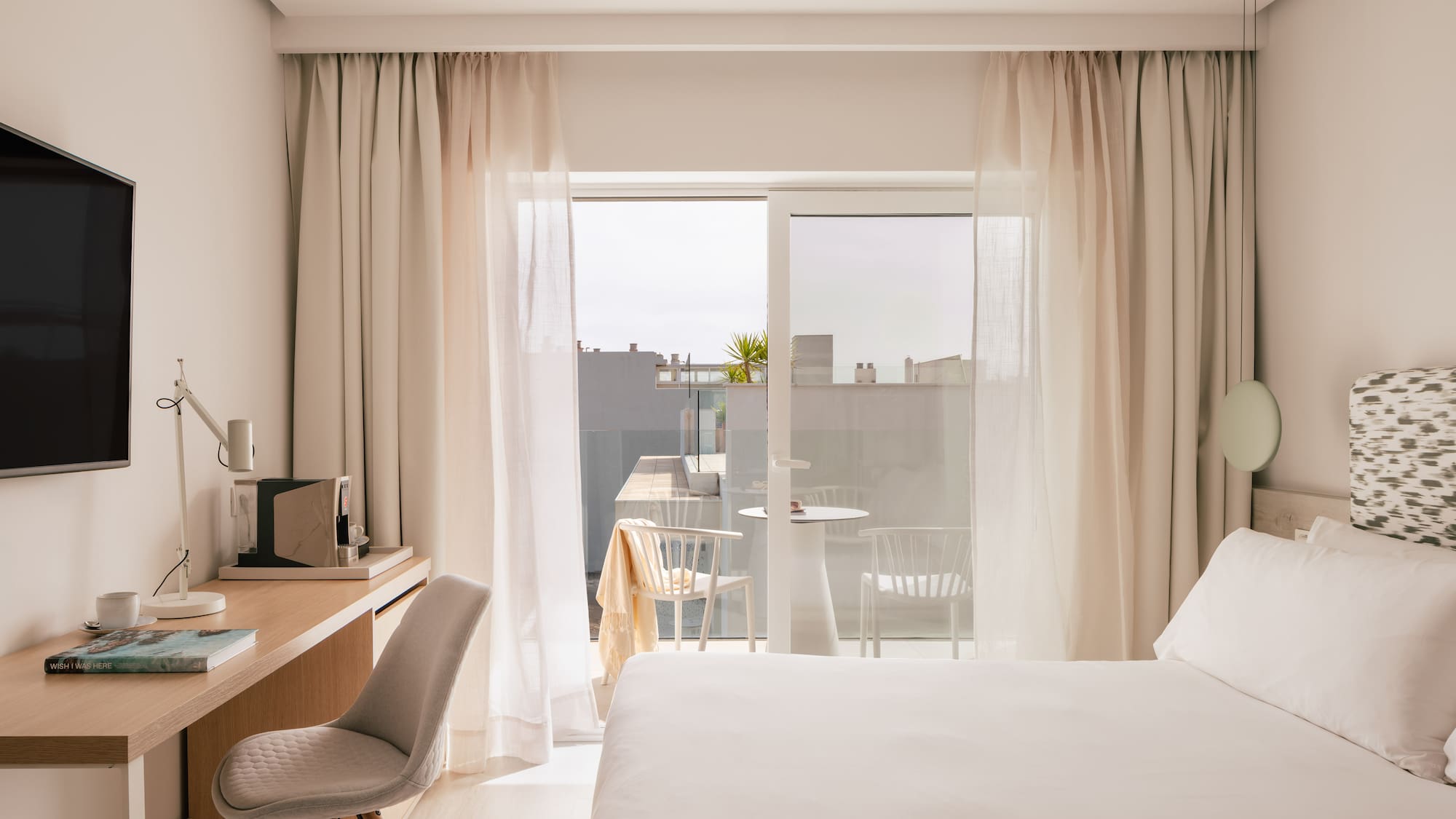 Bright, modern hotel room with bed, desk, and balcony.