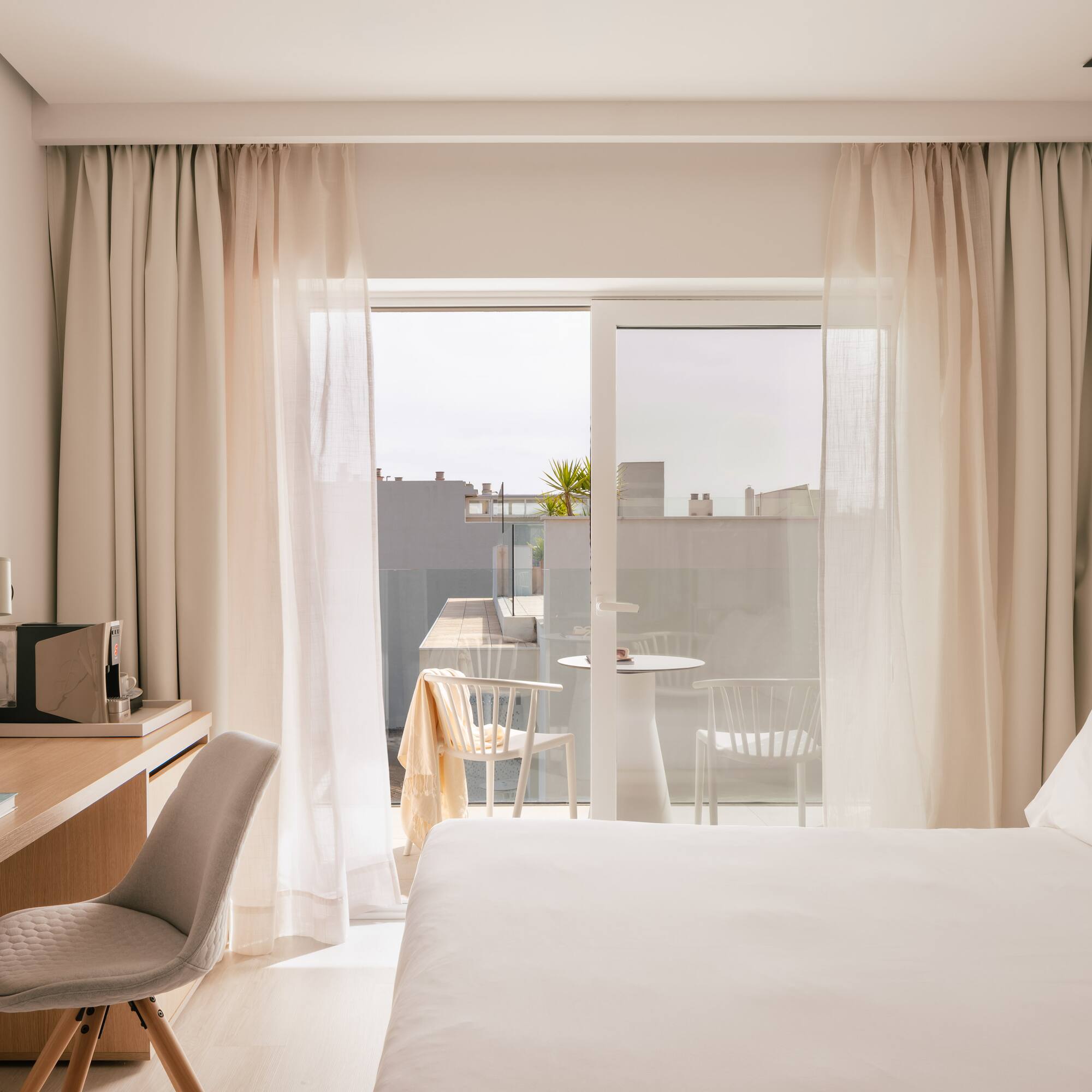 Bright, modern hotel room with bed, desk, and balcony.