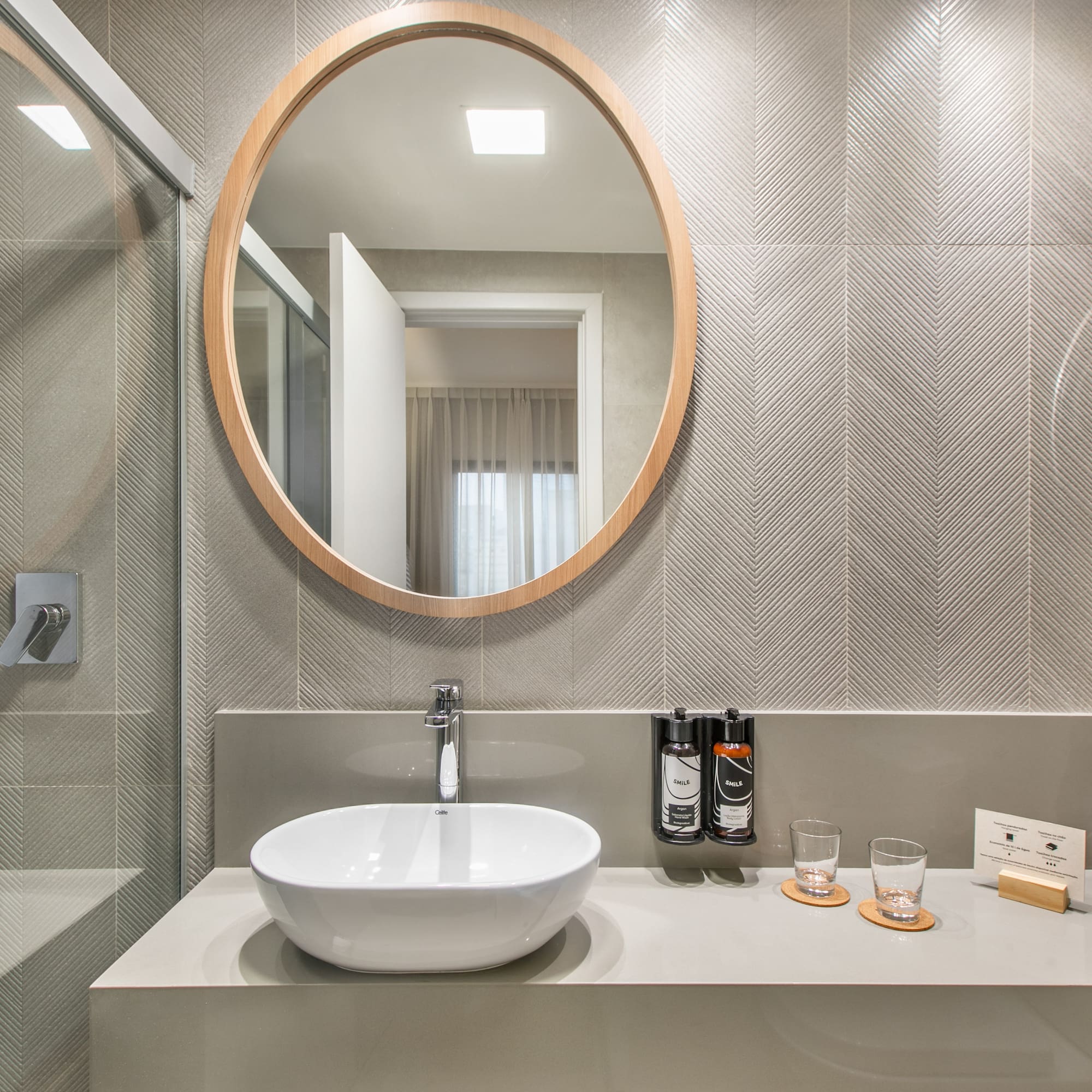 Baño moderno: espejo redondo, lavabo sobre encimera gris, azulejos chevron.