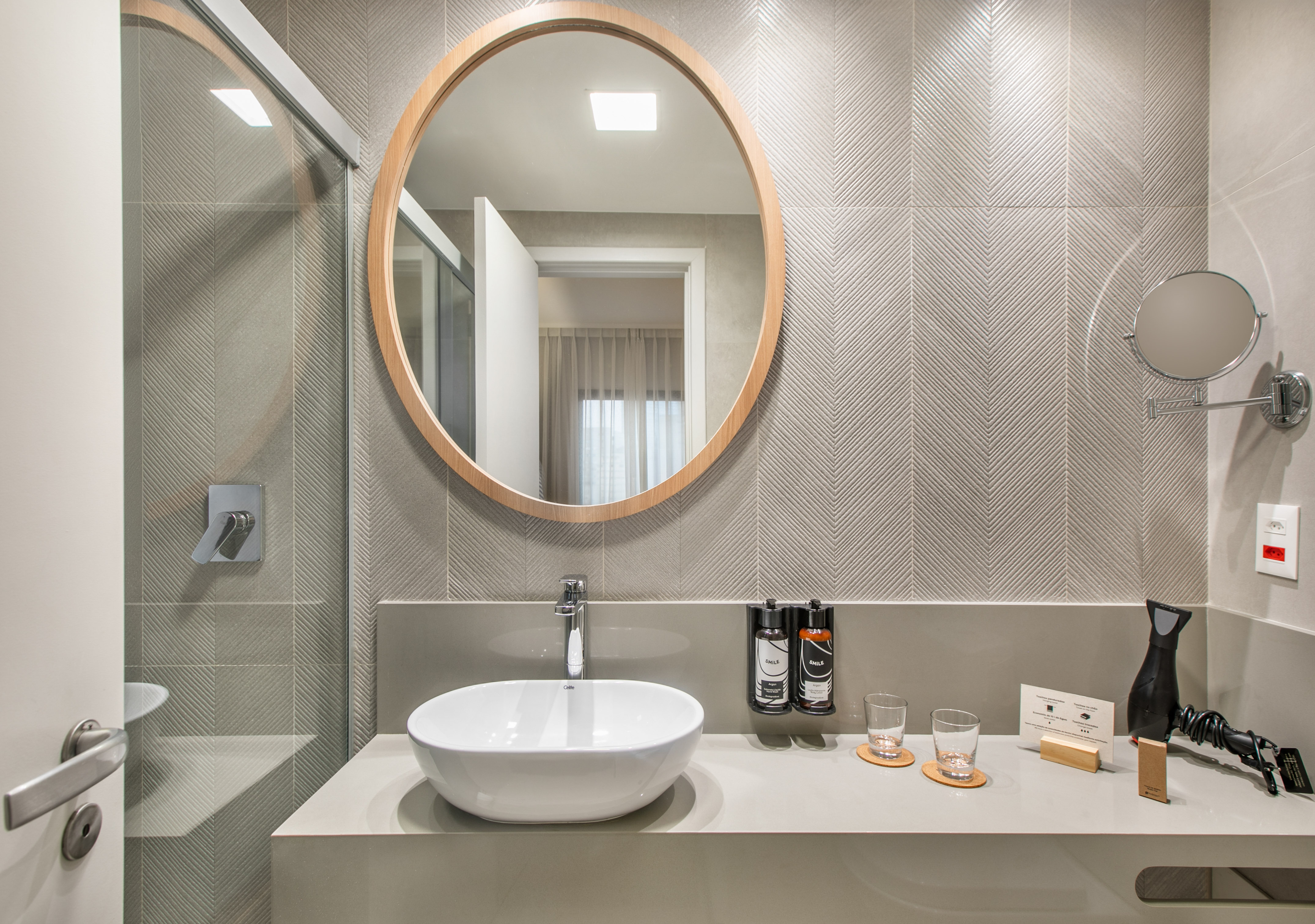 Baño moderno: espejo redondo, lavabo sobre encimera gris, azulejos chevron.