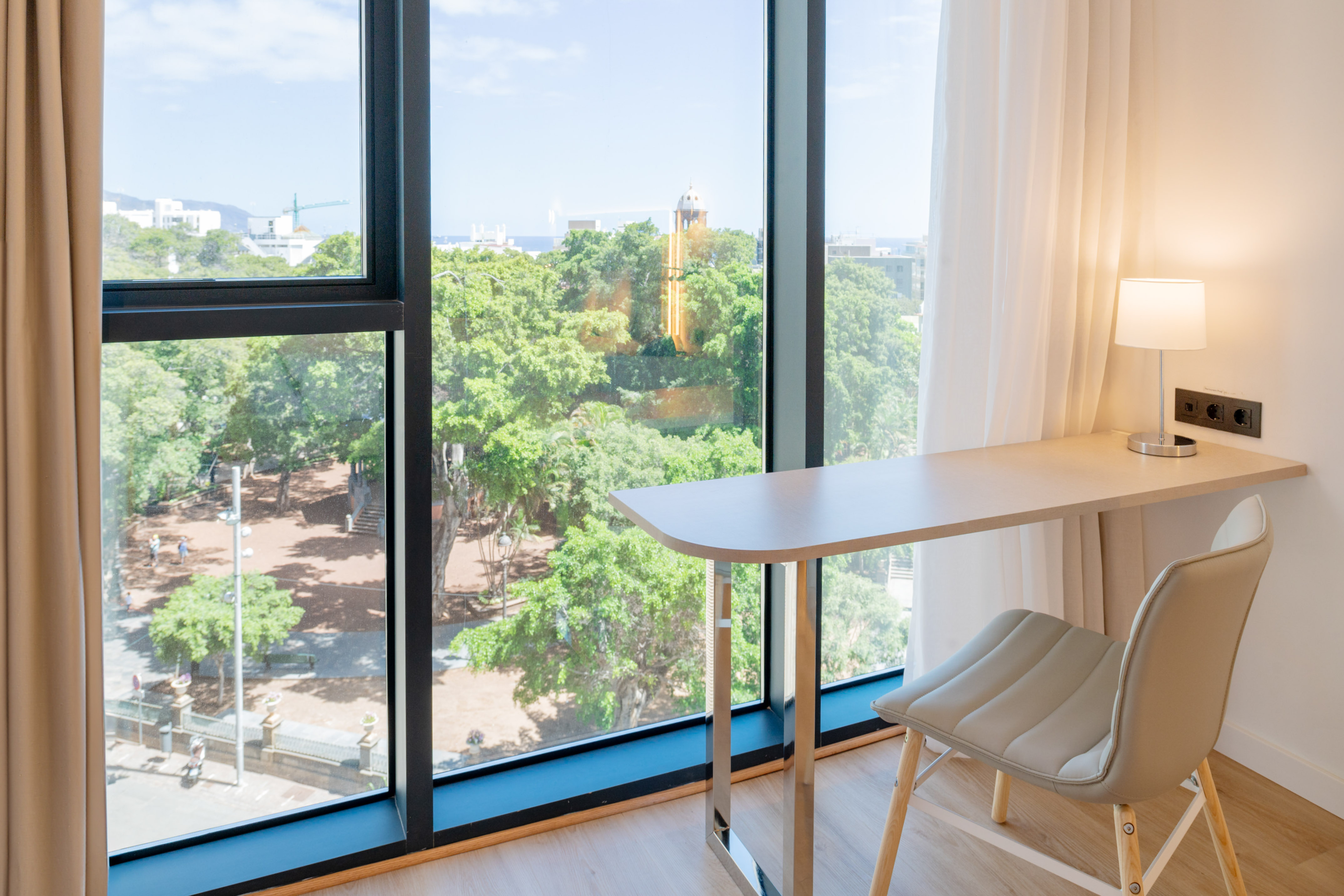 Modern hotel room workspace with desk, chair, and large window park view.