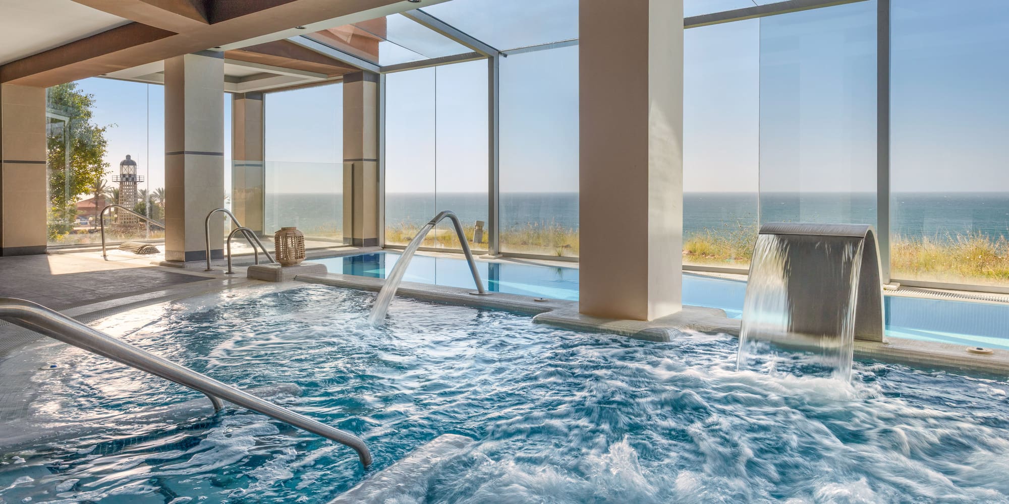 Oceanfront spa pool with bubbling water, waterfall, and a distant lighthouse.