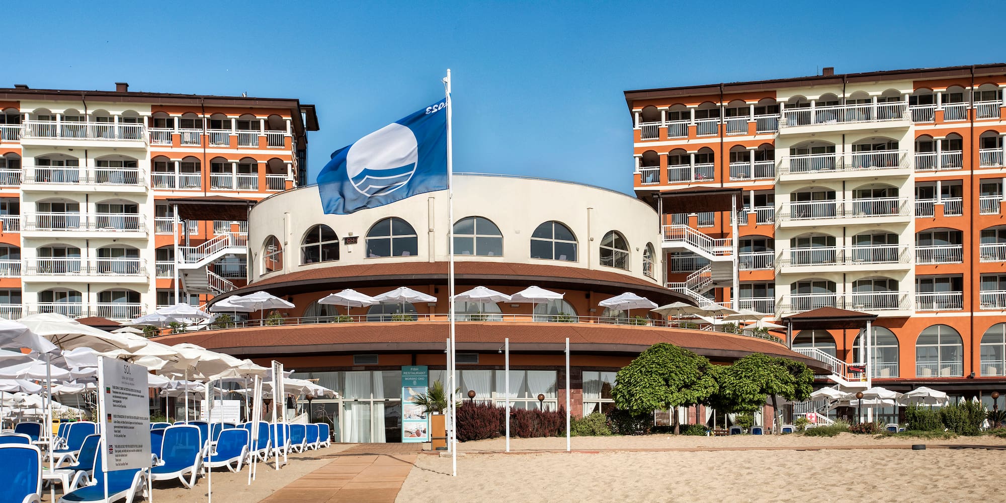a building with a flag and umbrellas on a beach