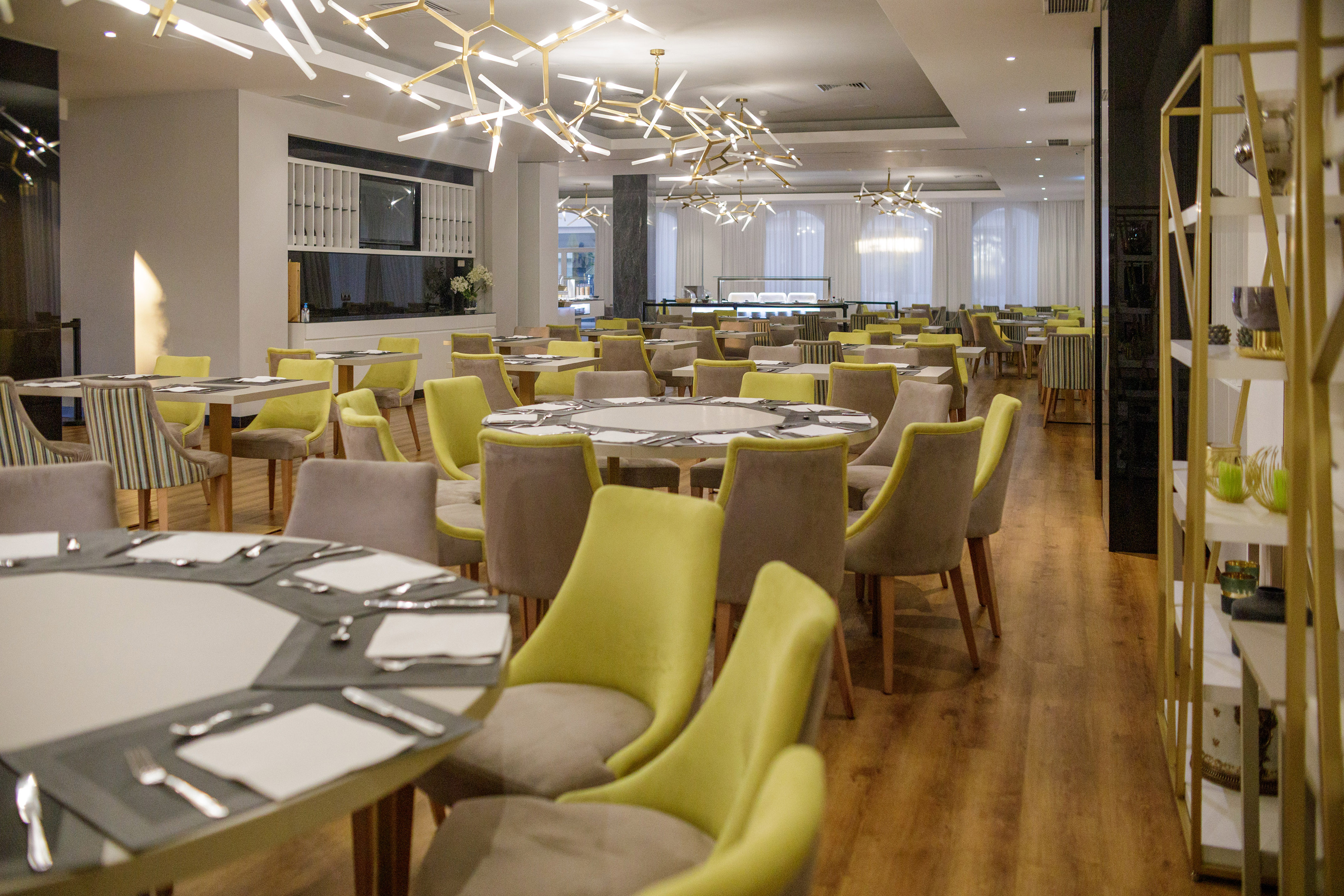 Contemporary dining room with green chairs, geometric chandeliers, and buffet area.