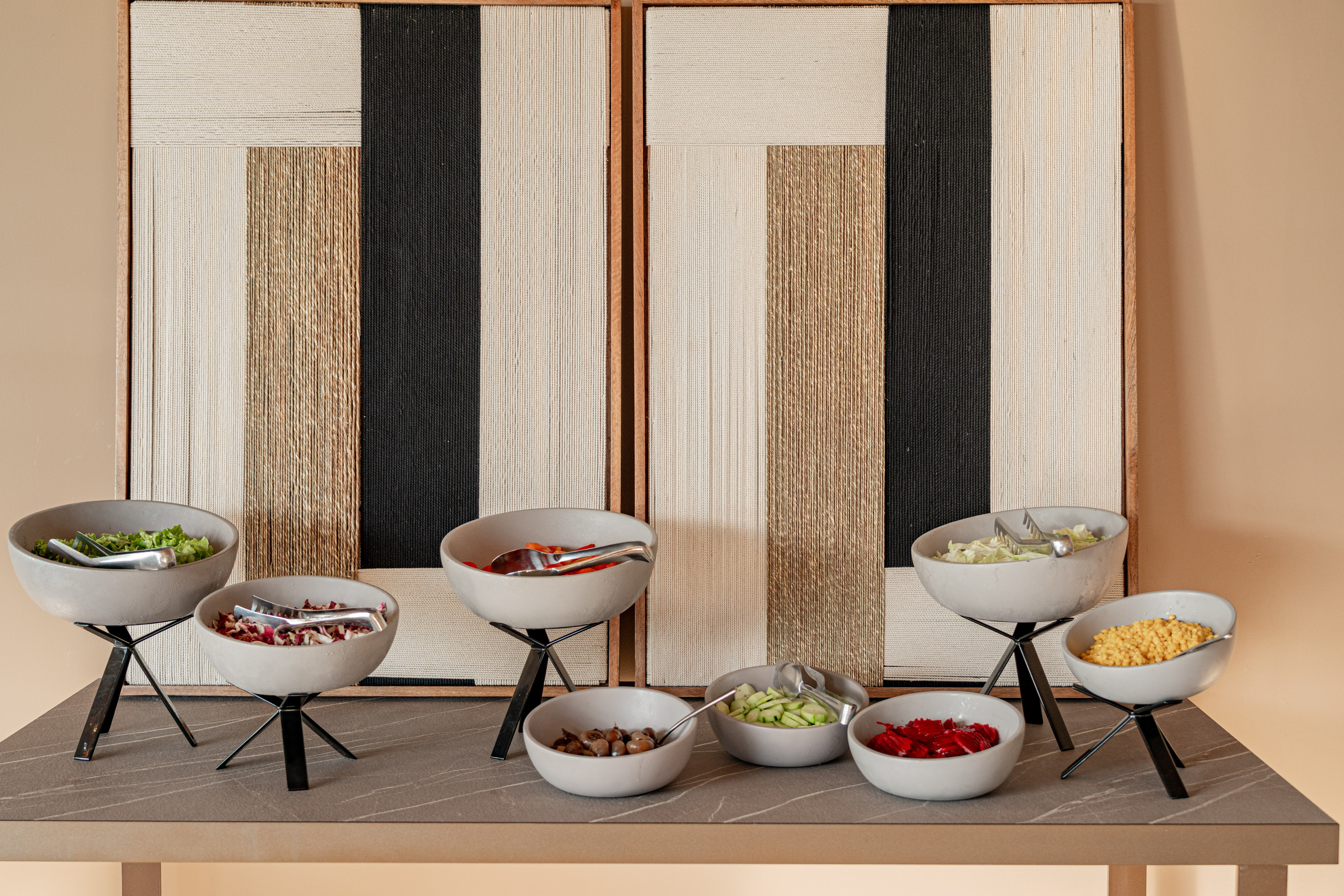 Modern buffet salad bar with fresh ingredients in various grey bowls.