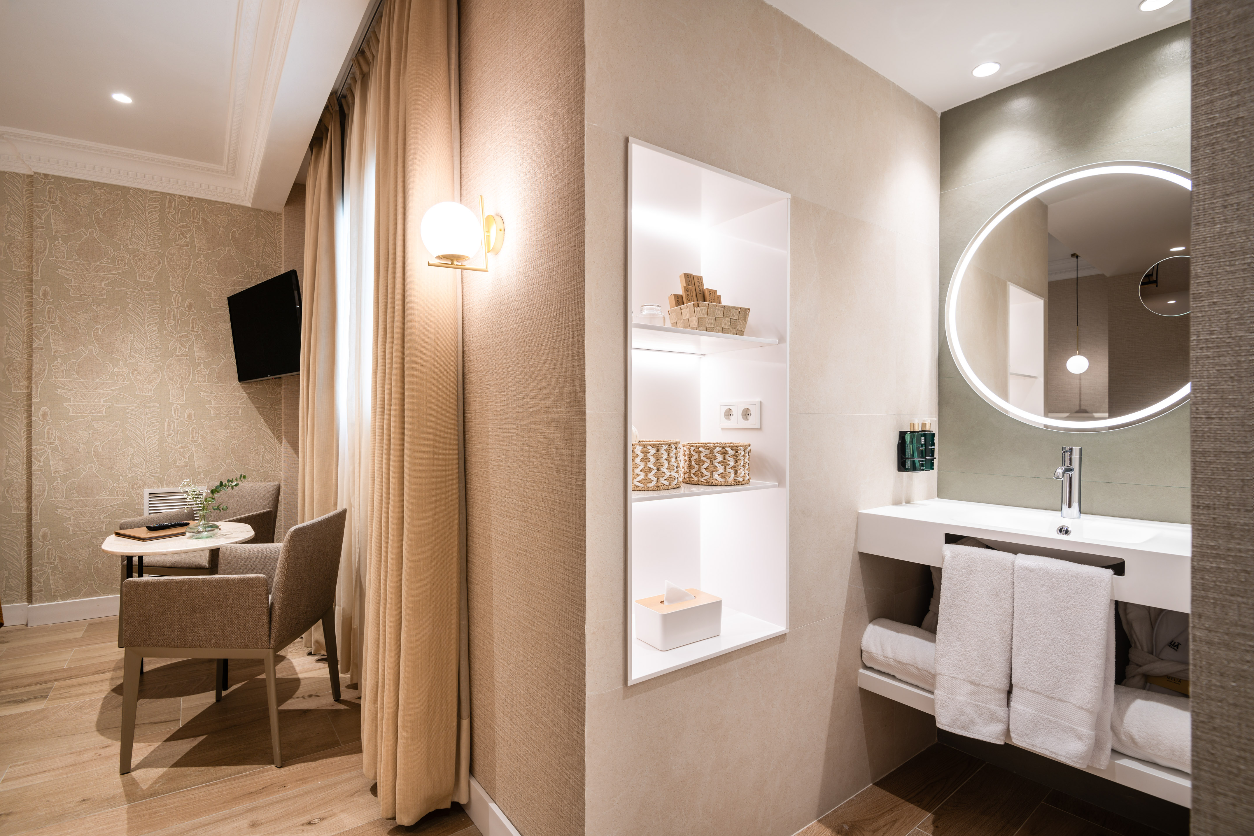 Modern hotel suite with vanity, illuminated mirror, and lounge area.