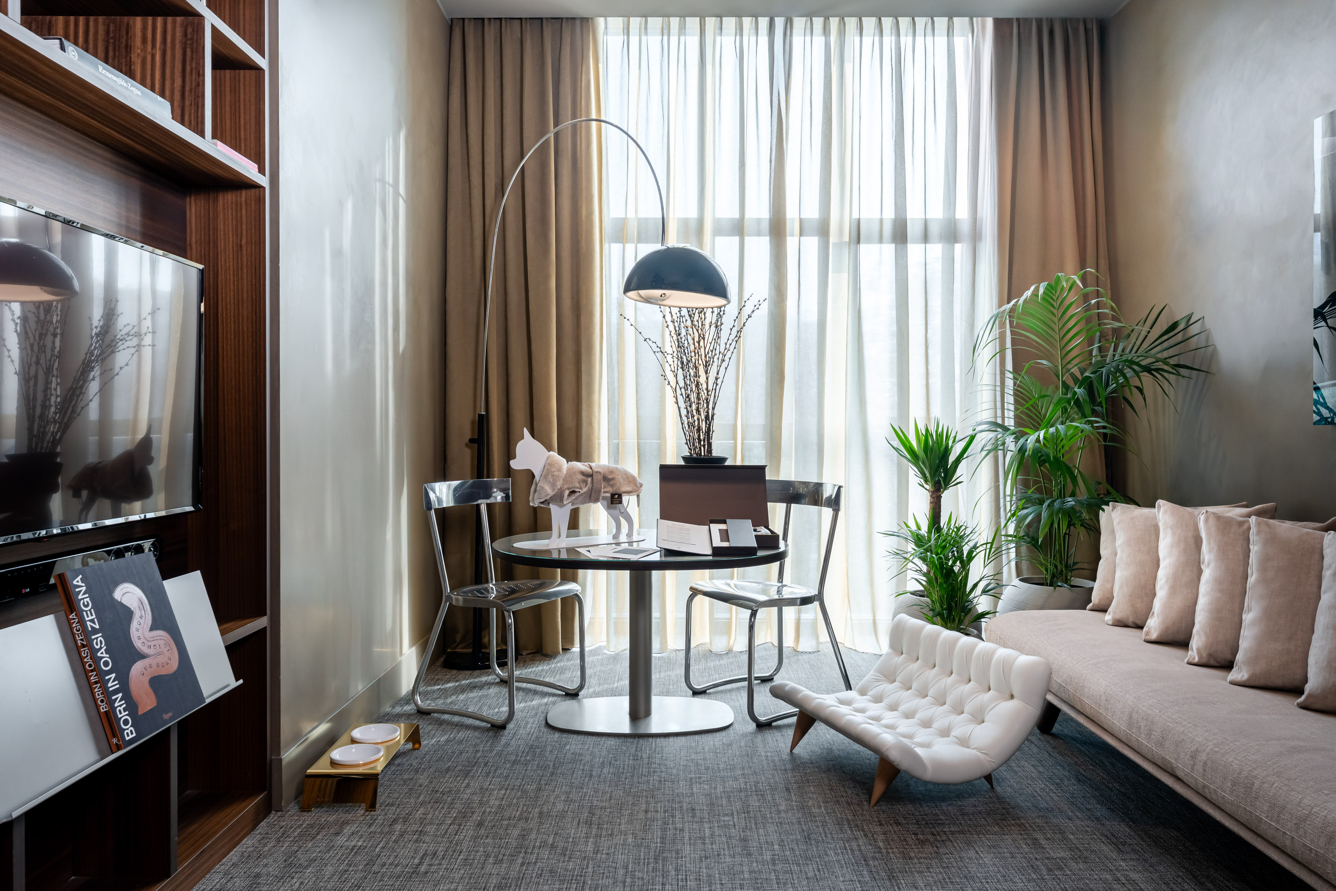Contemporary hotel suite with sofa, dining area, arc lamp, and plants.