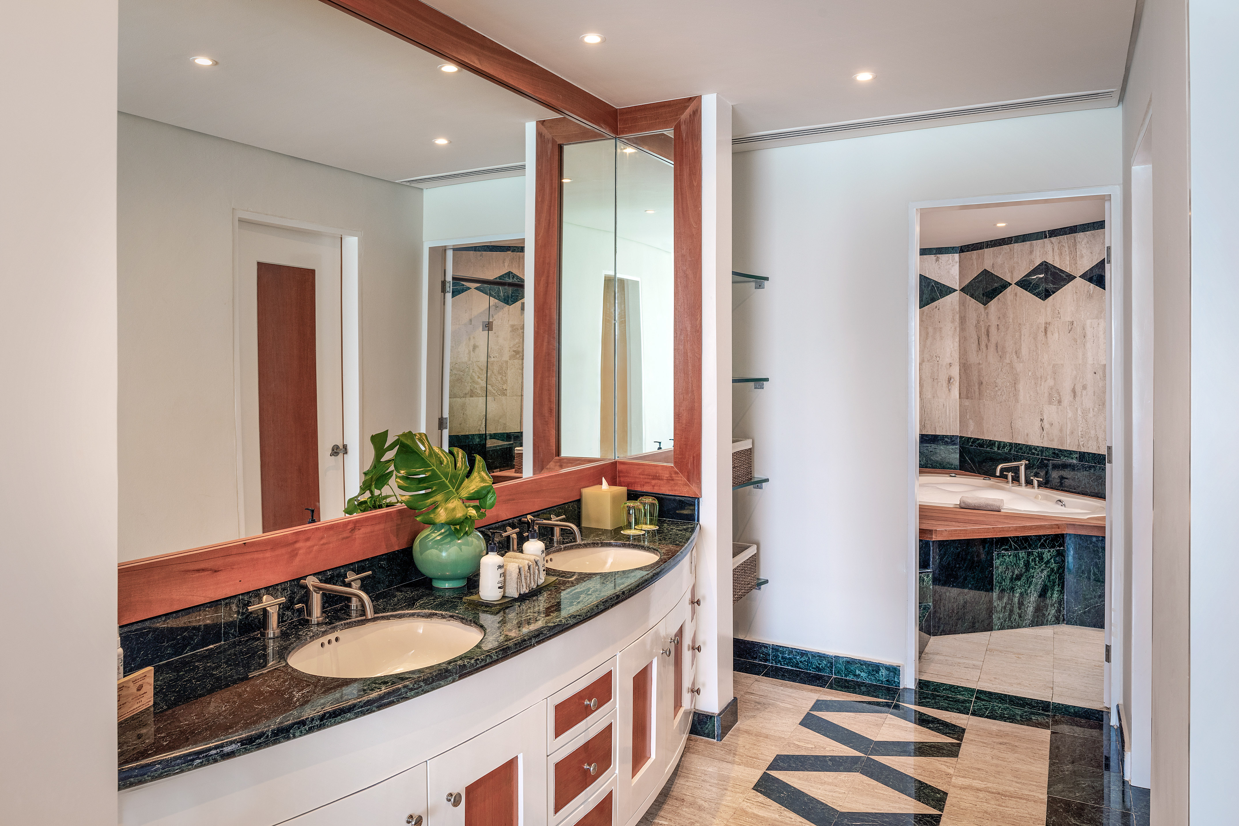 Double vanity bathroom with dark marble countertop, wood accents, and geometric tile.