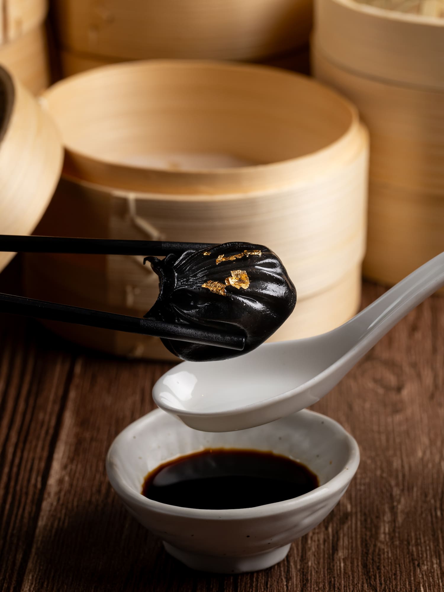 a pair of chopsticks holding a black object with gold leaf on a spoon
