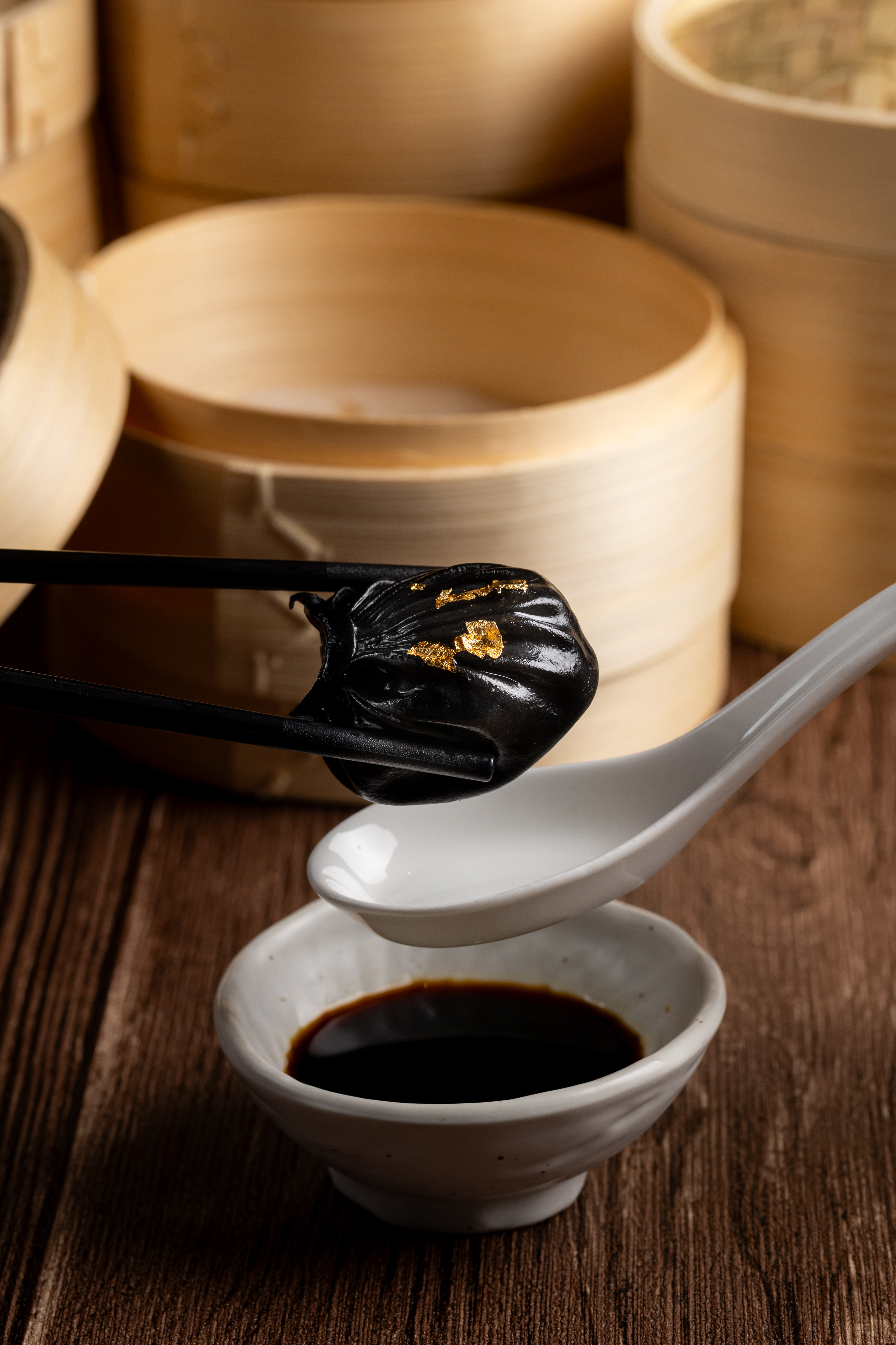 a pair of chopsticks holding a black object with gold leaf on a spoon
