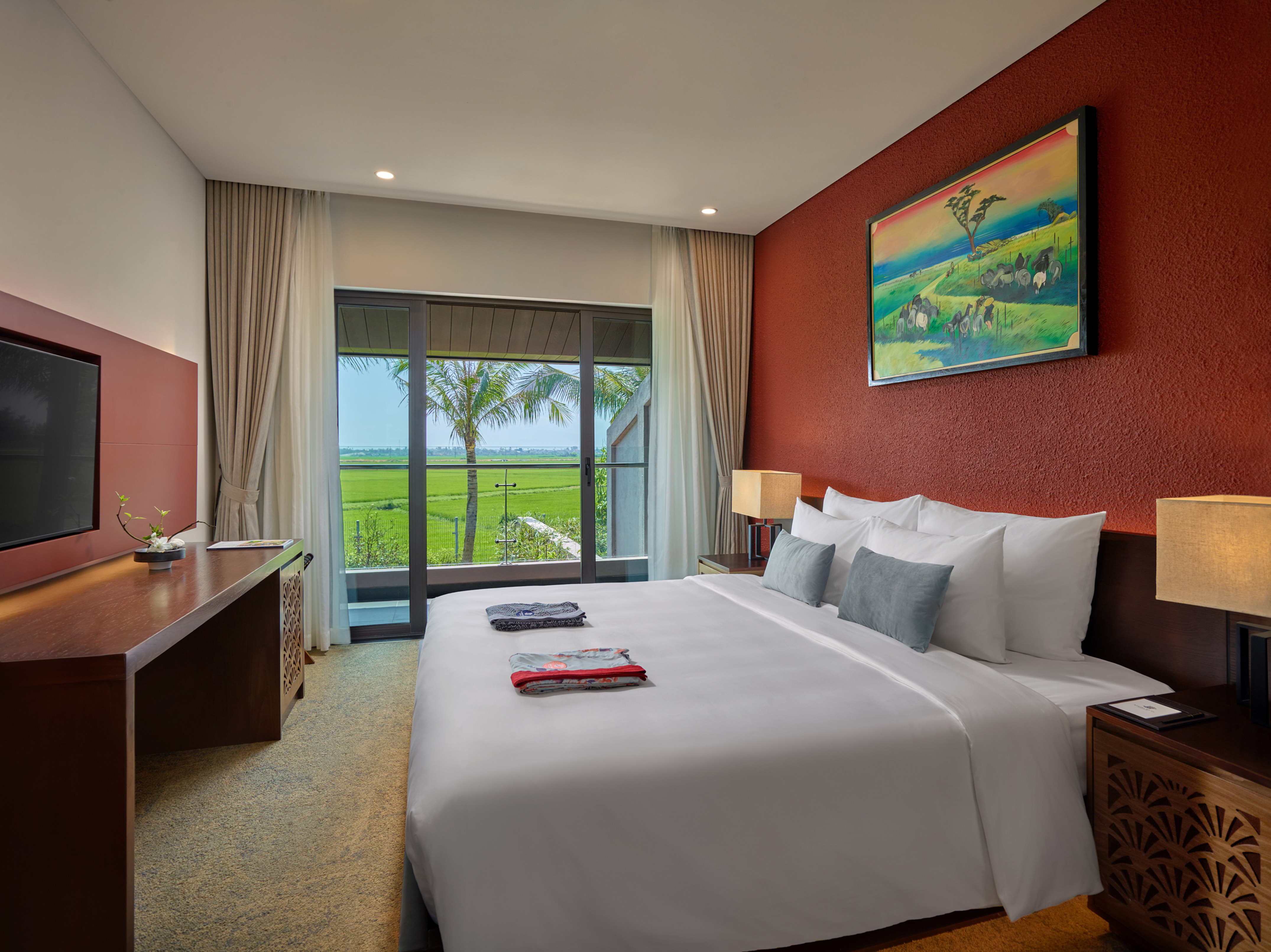 Modern bedroom with red wall, comfortable bed, and scenic rice field view.